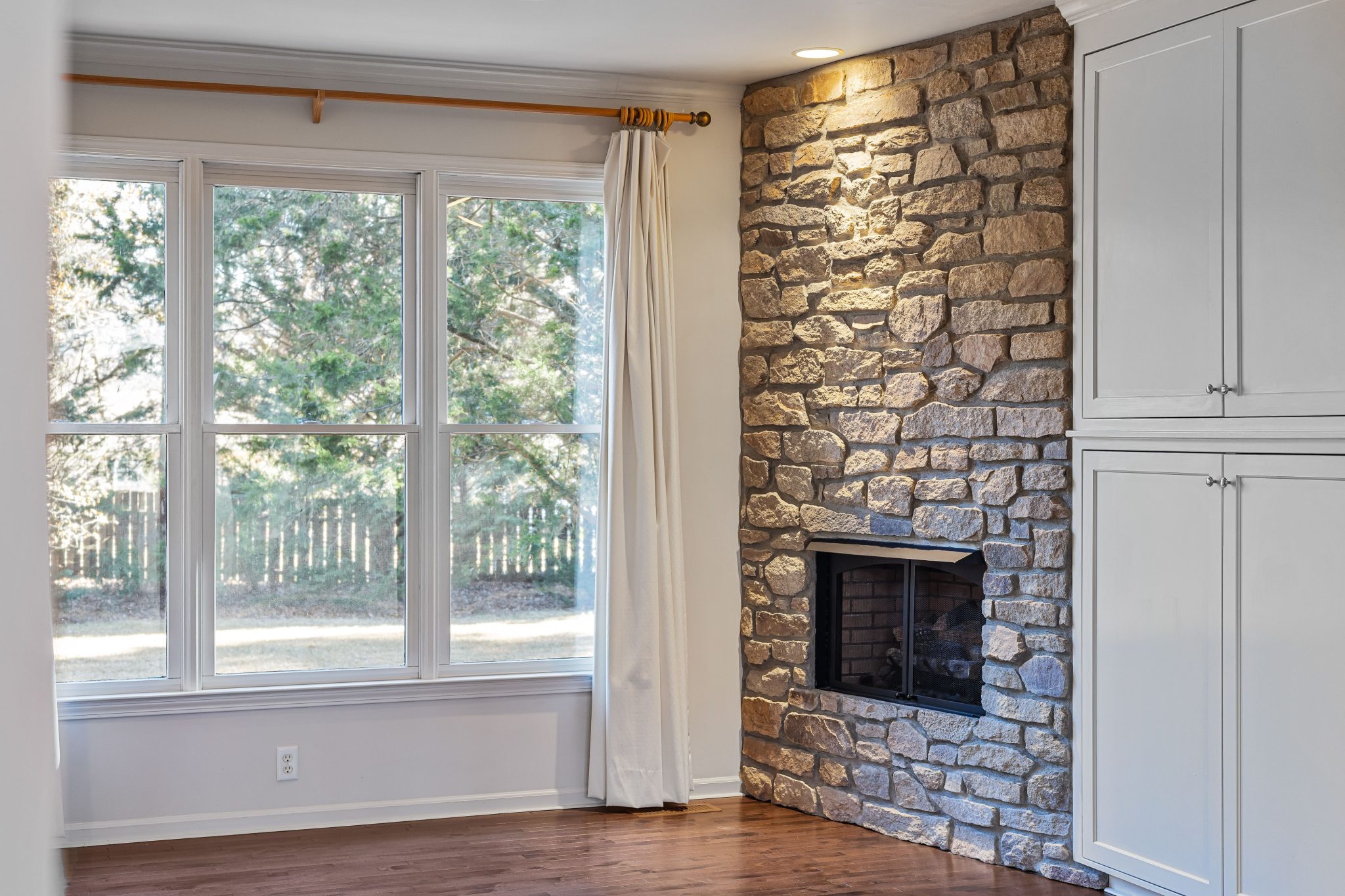 Bright modern living room featuring a stone wall fireplace and expansive windows with a view.