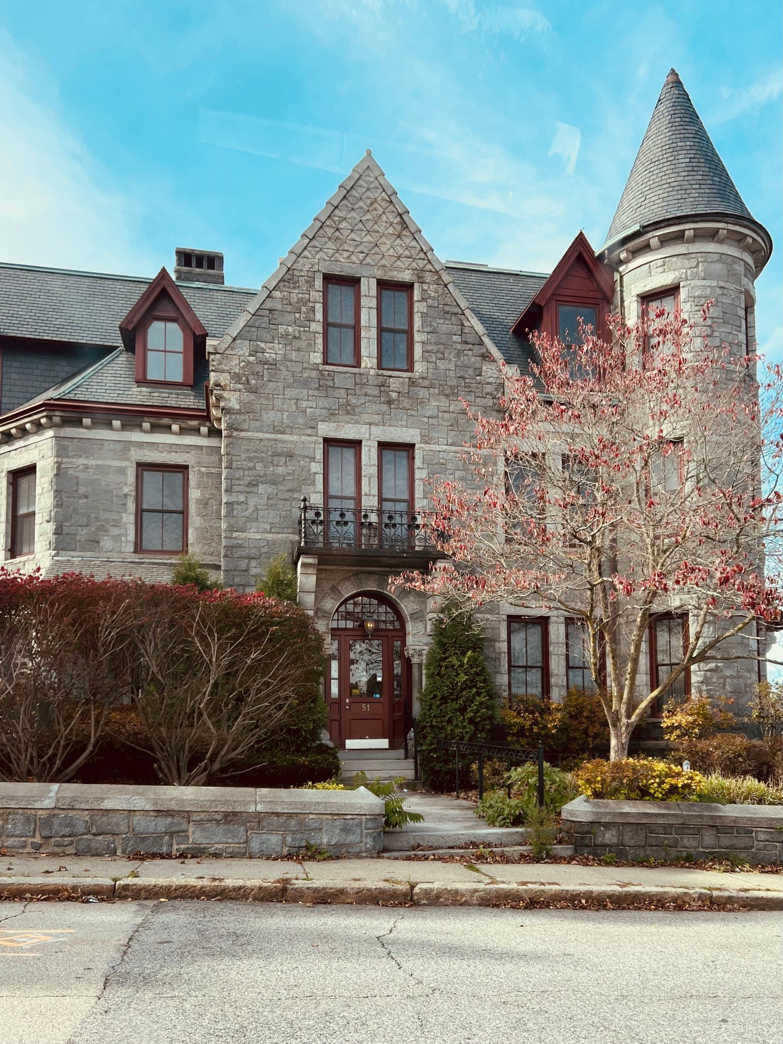 Charming historic mansion with a stone facade and turret beneath a clear blue sky.
