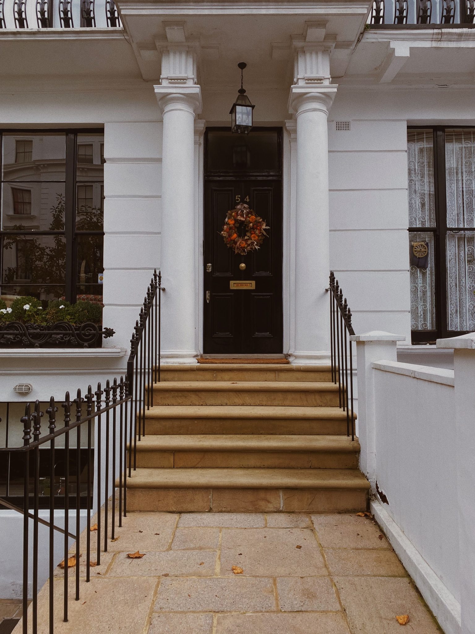 Charming townhouse entrance with columns, a black door, and autumn wreath.