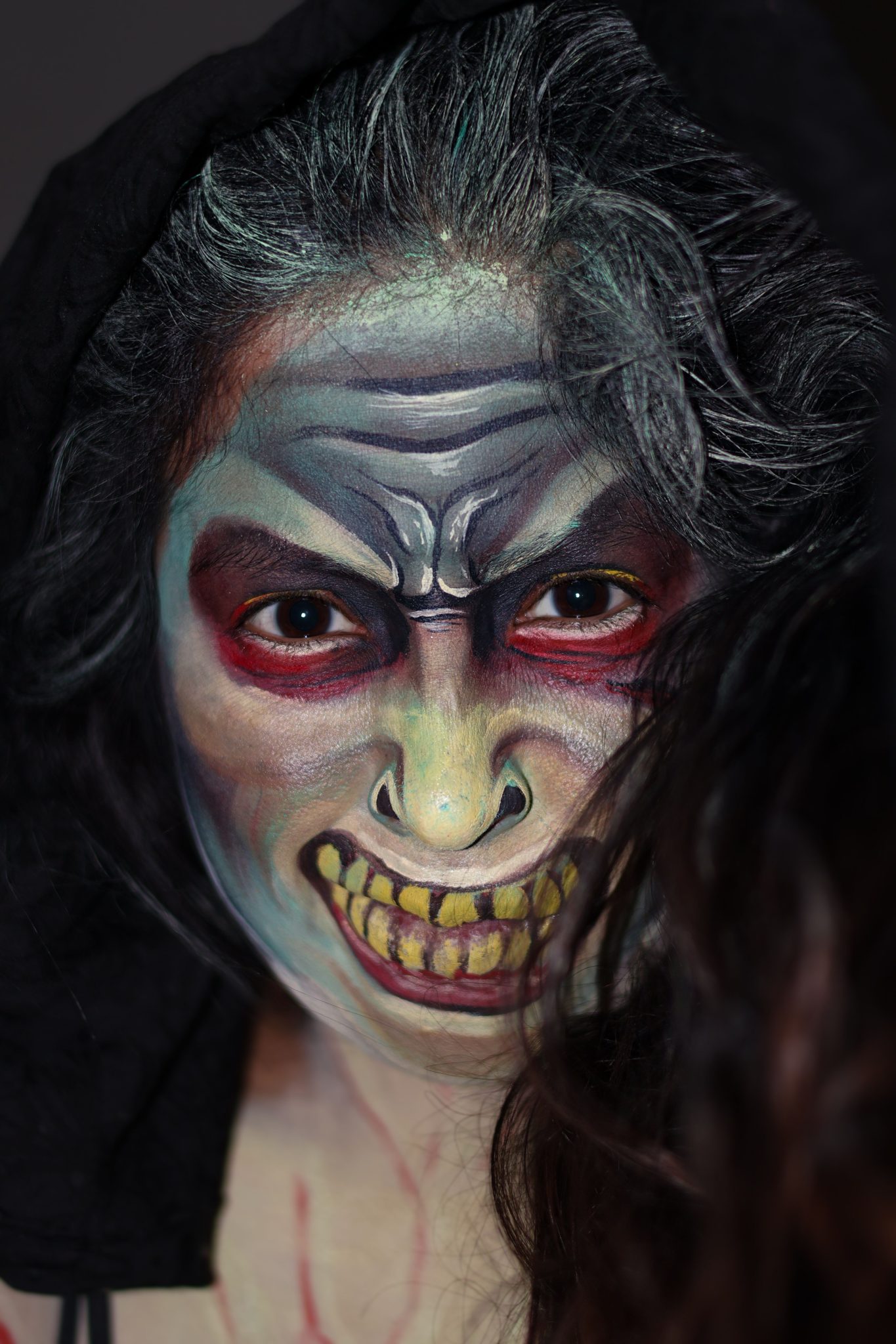 Chilling face paint of a demonic figure on a woman wearing a dark hood.