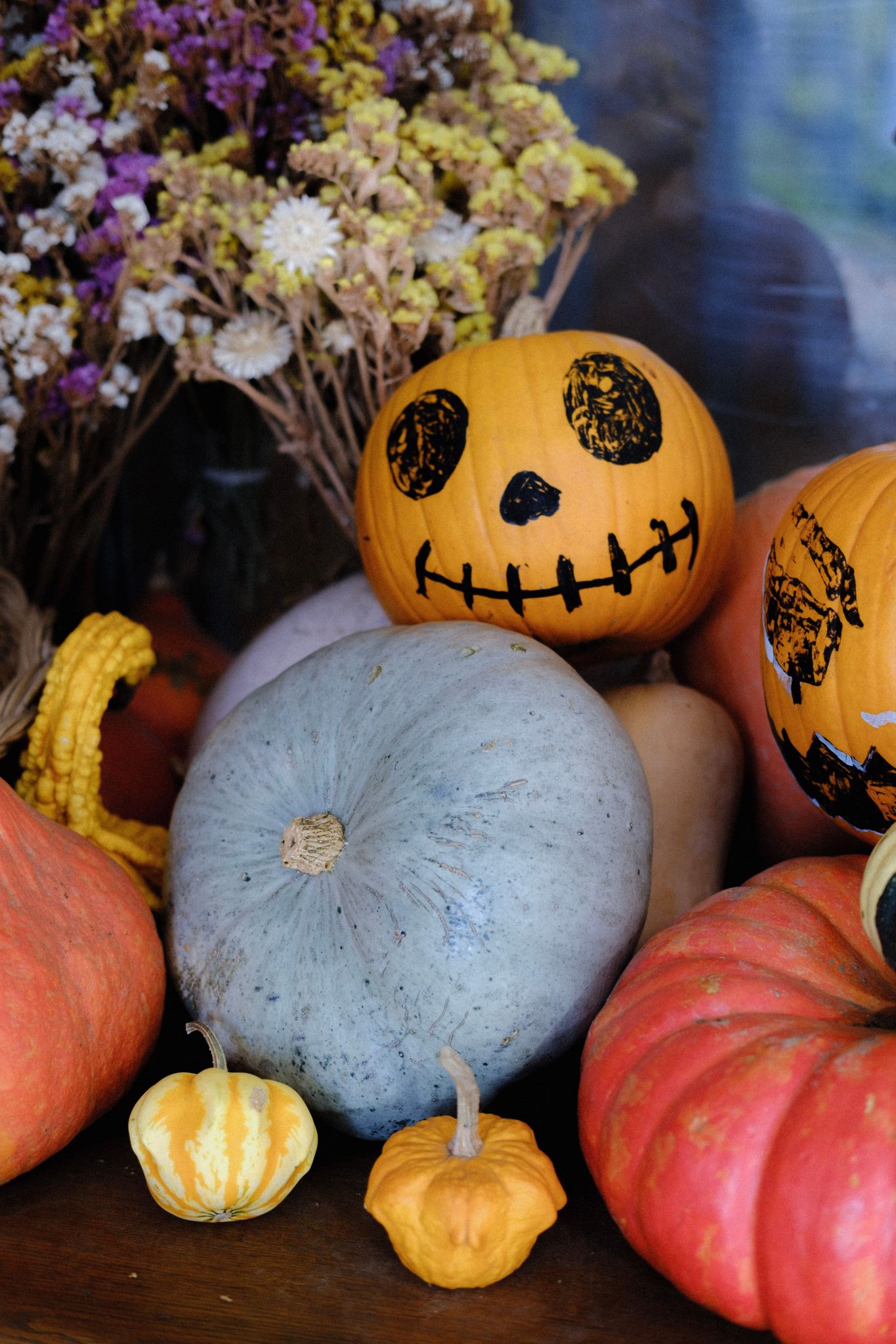 Colorful autumn display with hand-painted pumpkins and dried flowers, evoking a festive fall vibe.