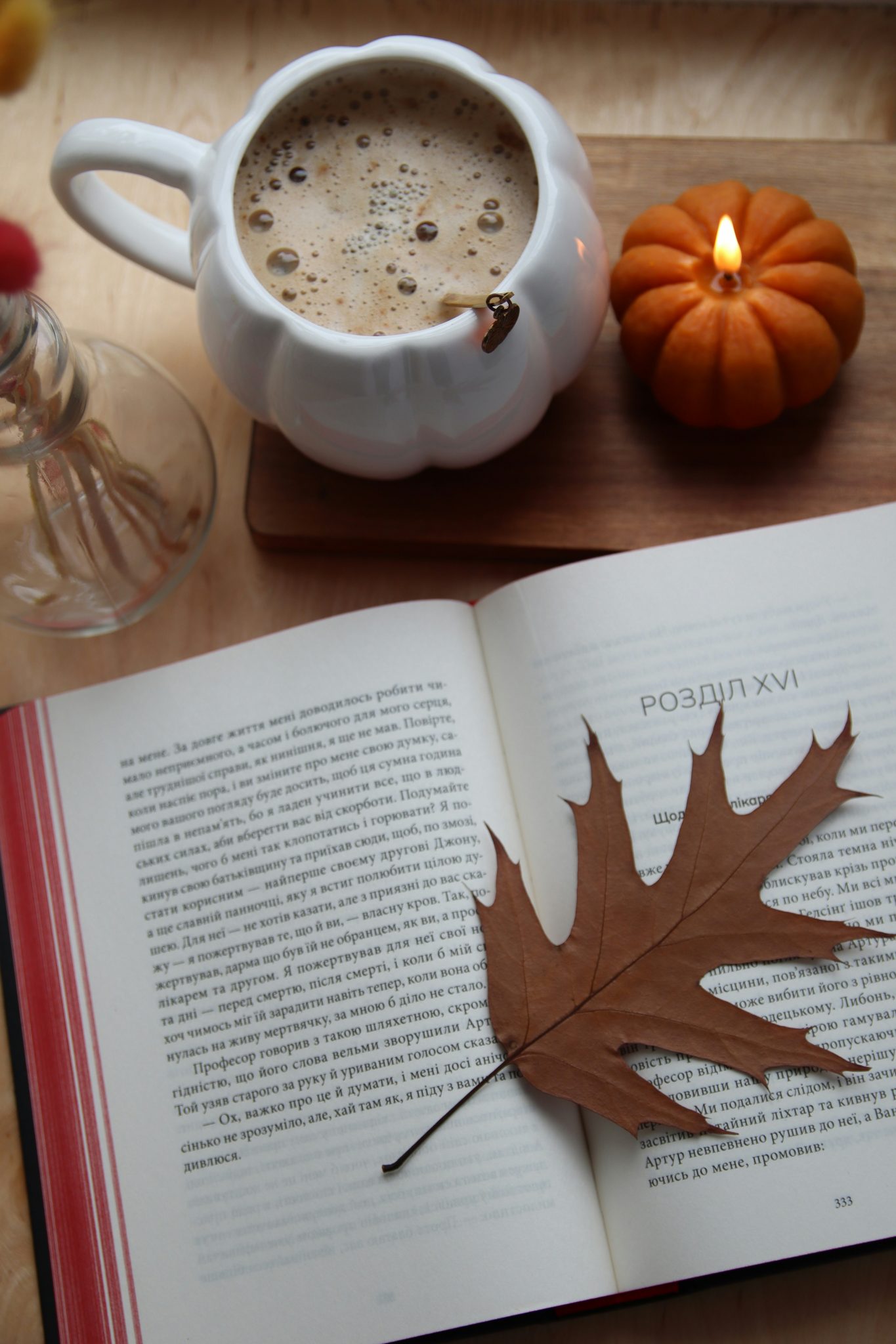 Cozy autumn scene with coffee, book, and pumpkin candle.