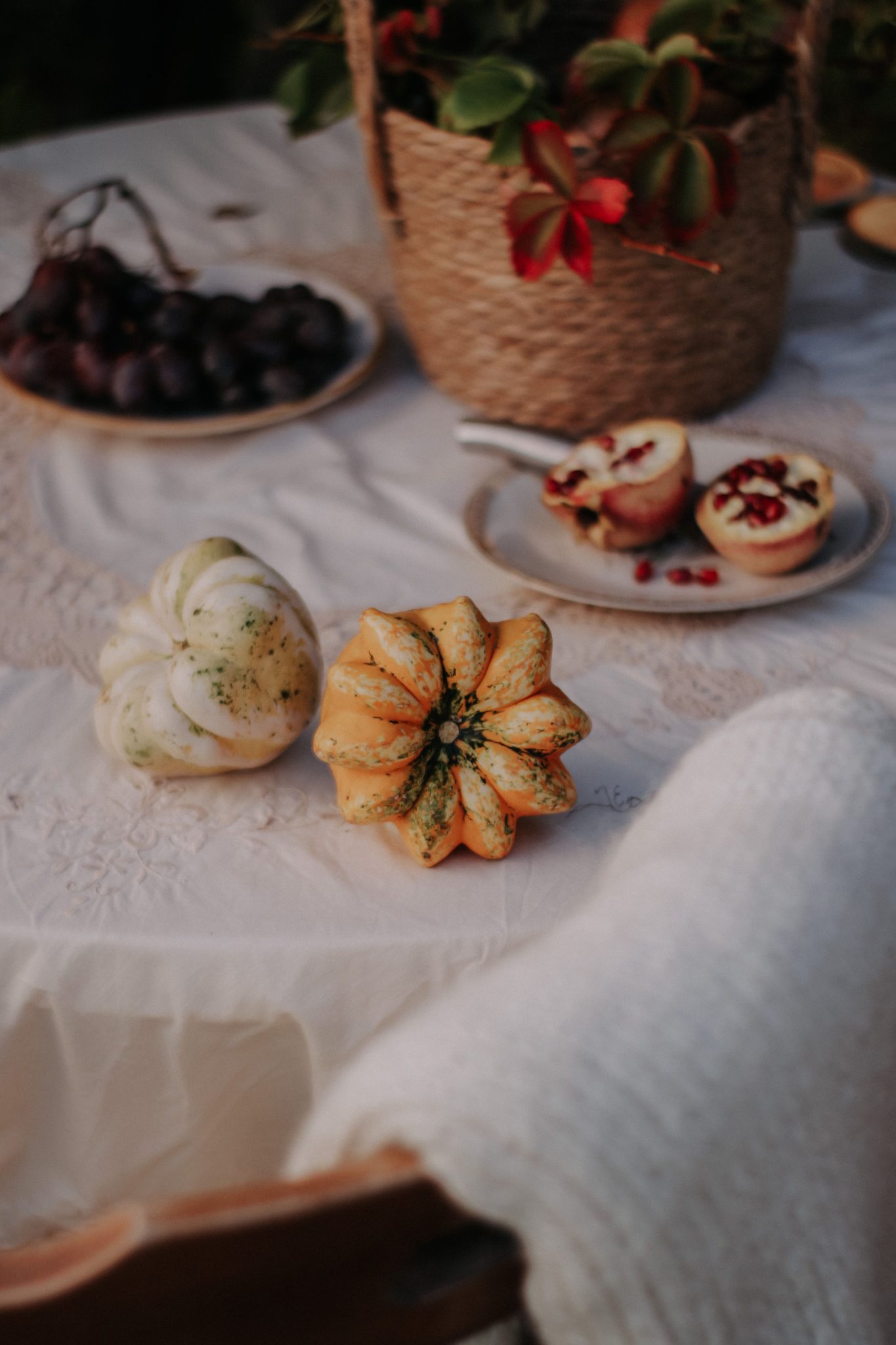 Cozy autumn table setting with fruits, gourds, and a wicker basket on a lace tablecloth.