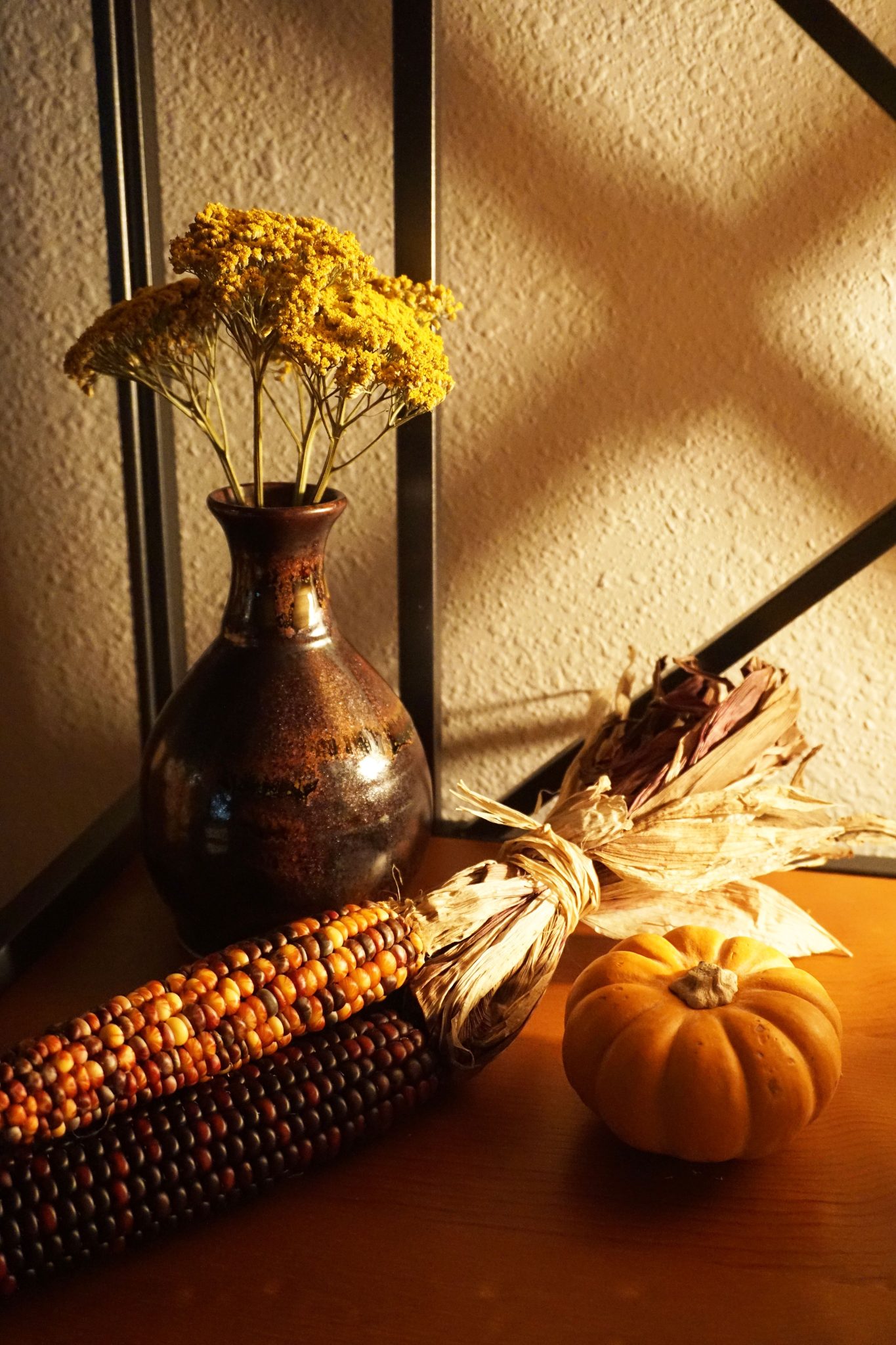 Cozy autumn tabletop arrangement featuring mini pumpkin, indian corn, and dried flowers in a vase.