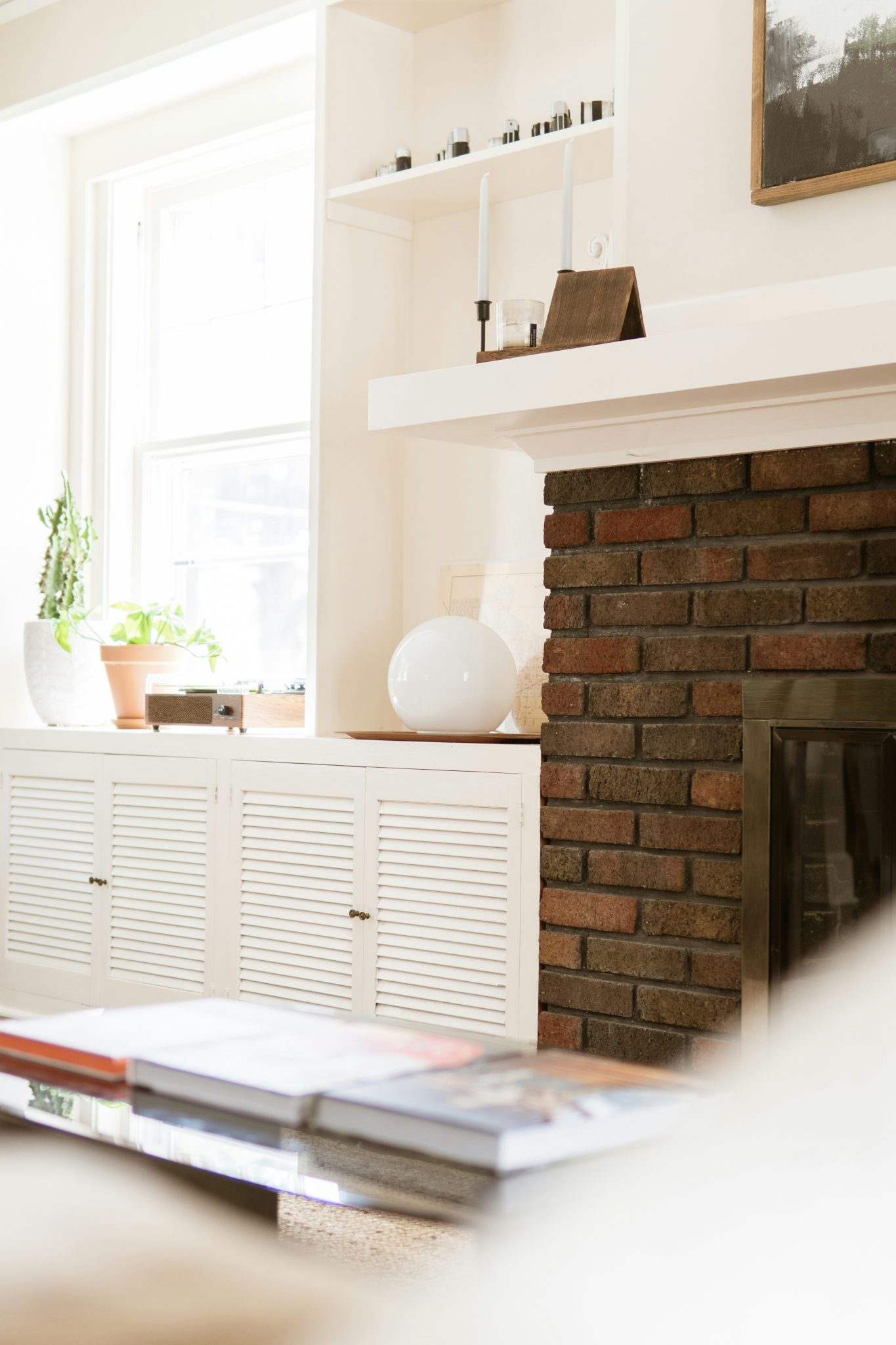 Cozy living room with brick fireplace, window, and decorative items.