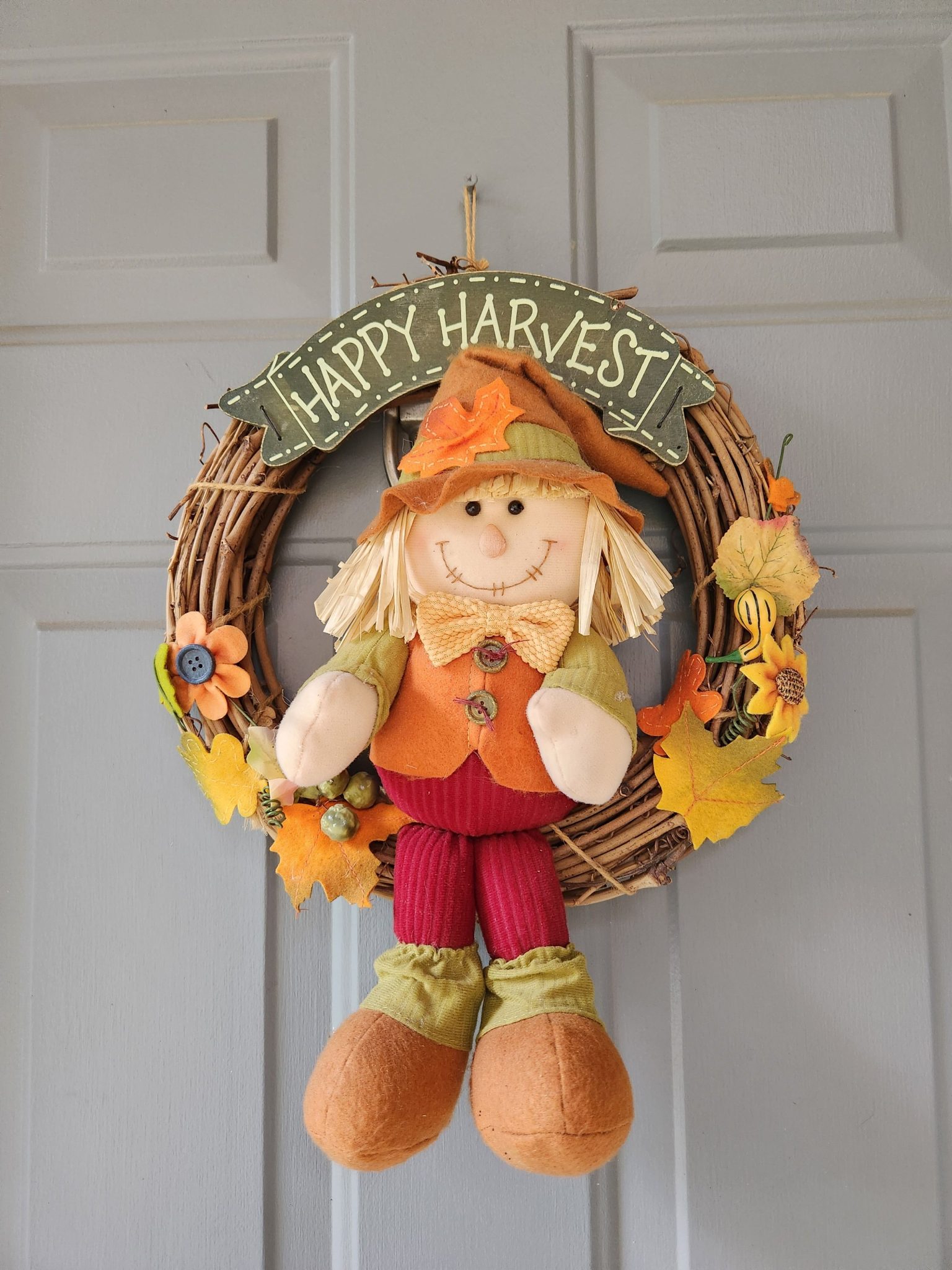 Decorative autumn wreath with a cheerful scarecrow and fall leaves, perfect for welcoming guests.