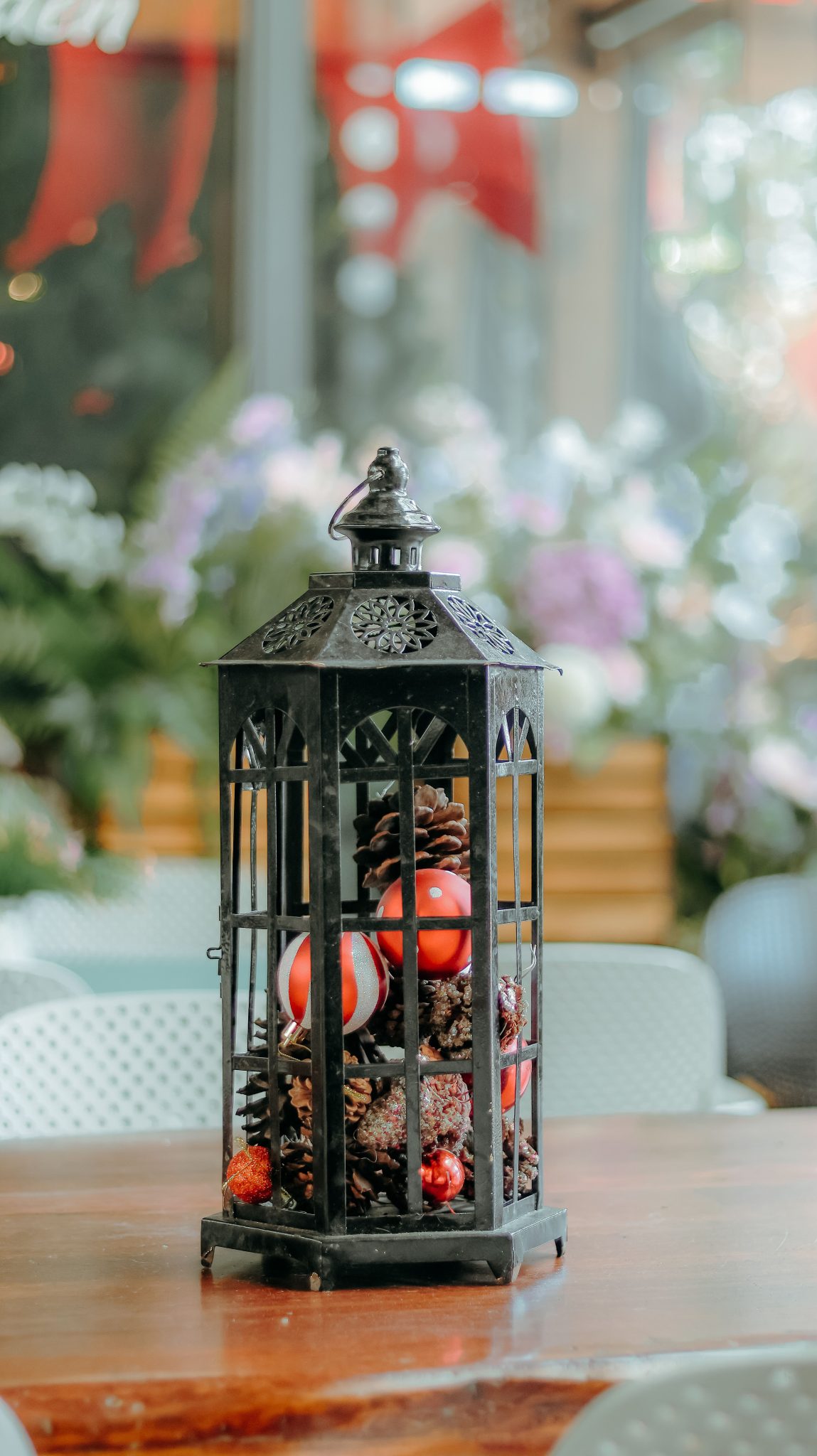 Decorative lantern filled with pinecones and red ornaments on a wooden table indoors.