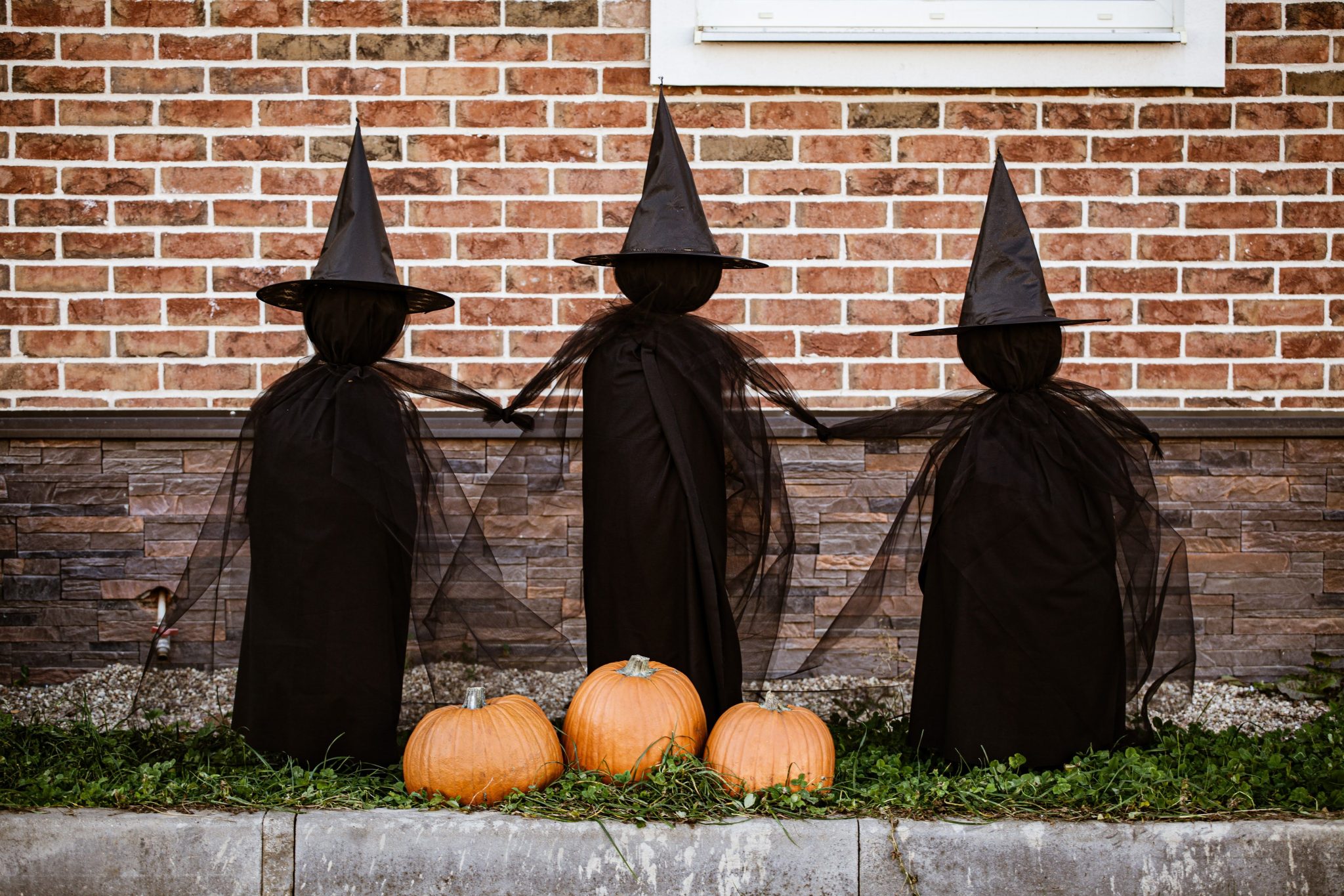 Decorative witch figures against a brick wall with pumpkins for Halloween ambiance.