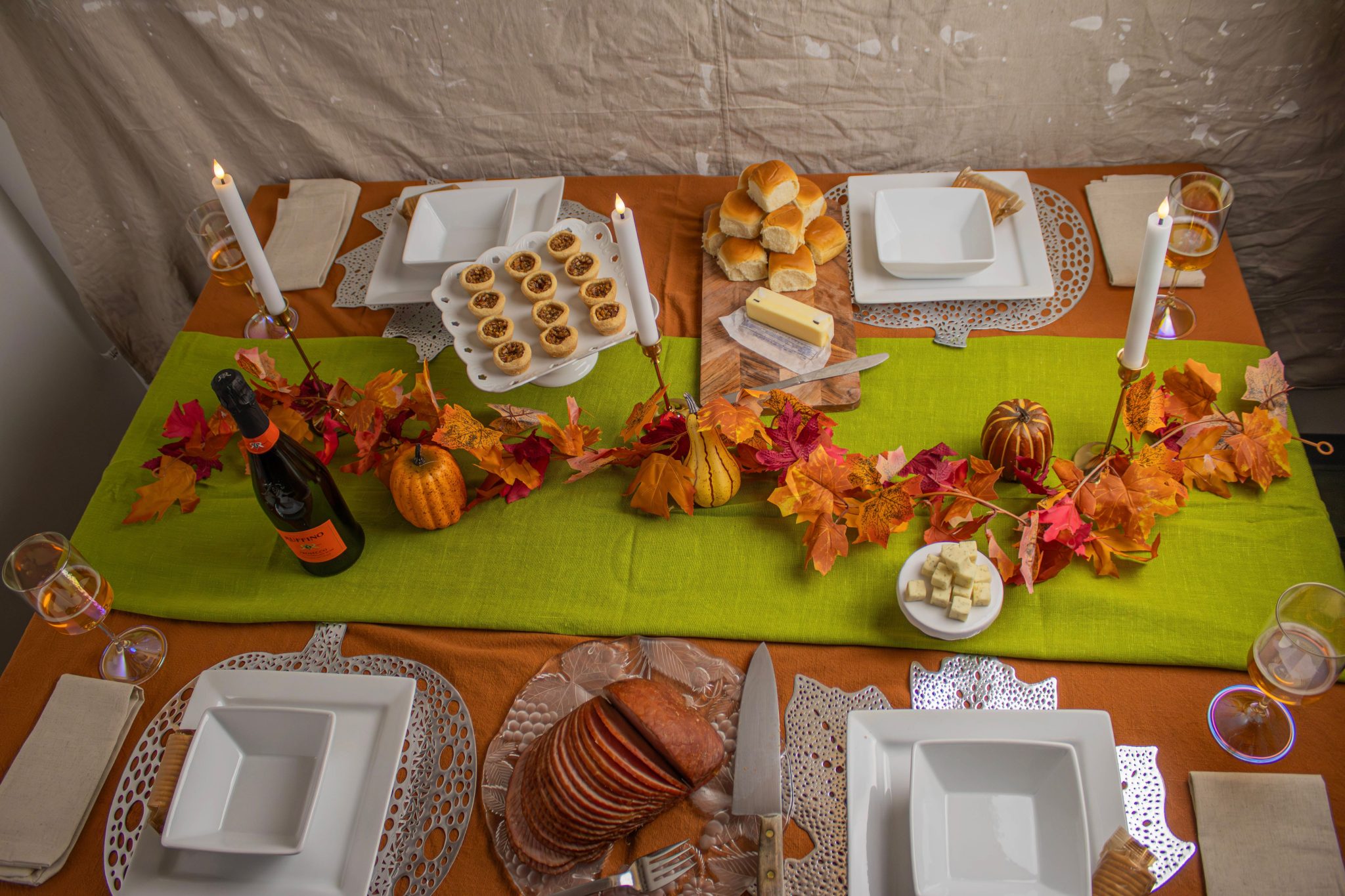 Elegant autumn themed table with pumpkins, candles, and seasonal leaves, set for a festive meal.