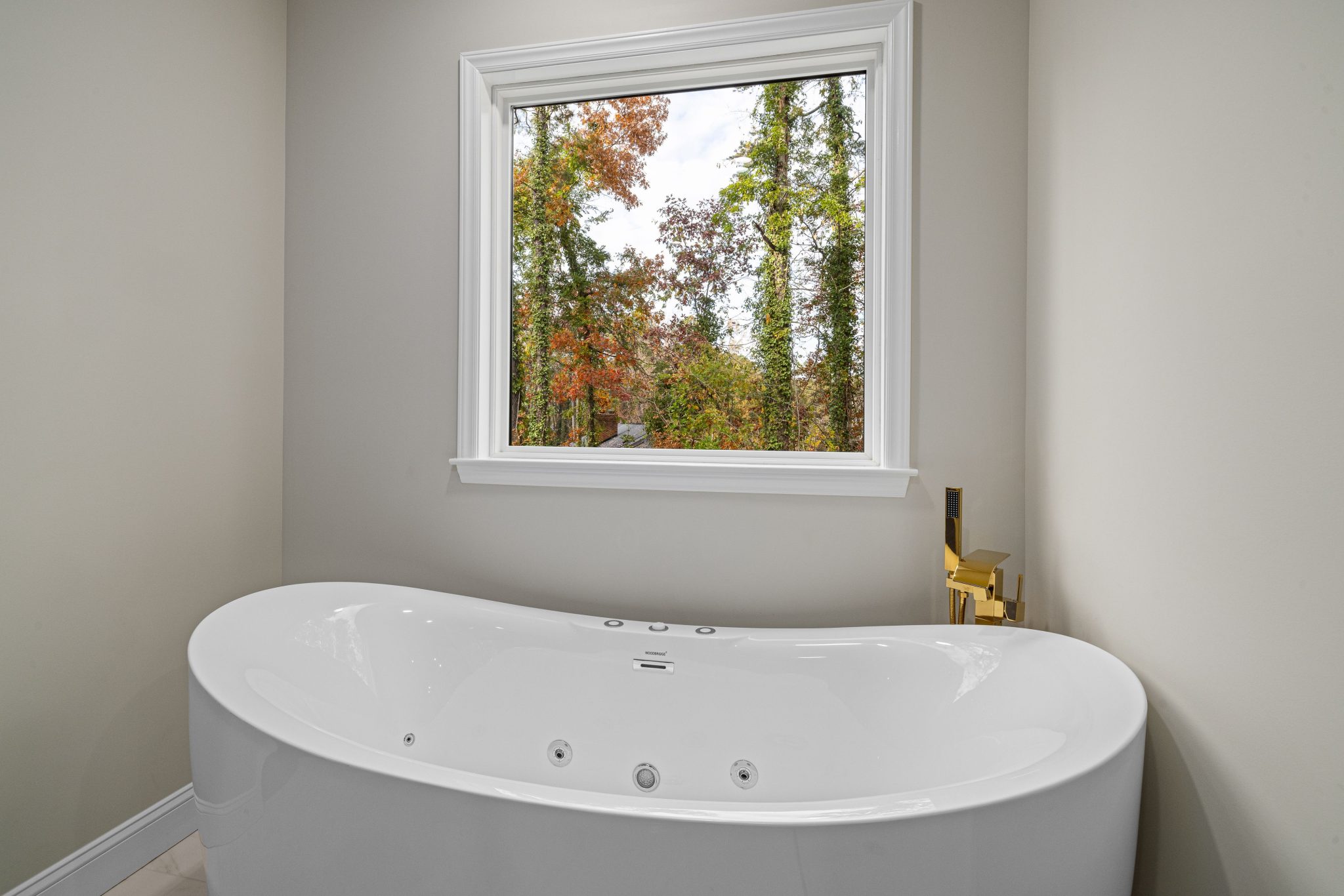 Elegant contemporary bathroom with a sleek bathtub and scenic autumn foliage view through the window.