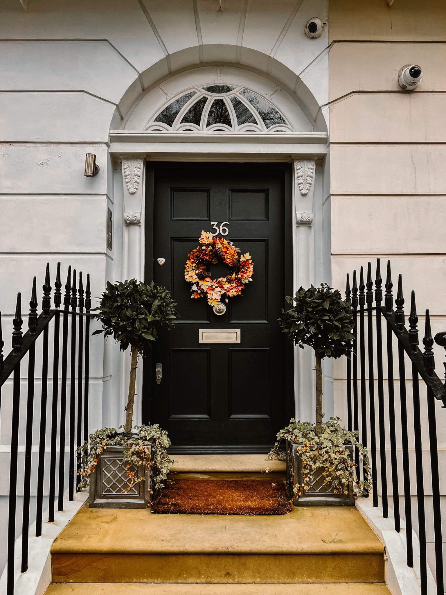 Elegant front door decorated with an autumn wreath and flanked by potted plants.