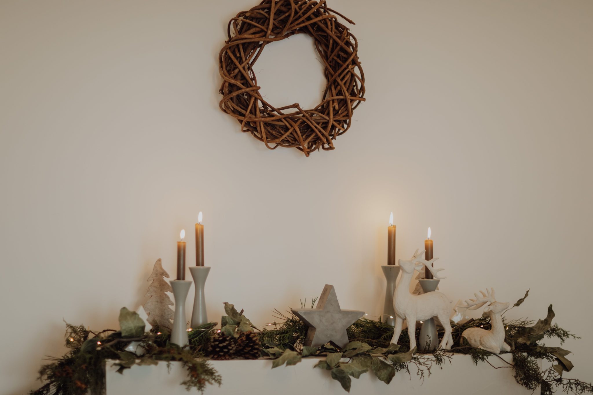 Elegant holiday mantle with candles and rustic wreath in warm lighting.