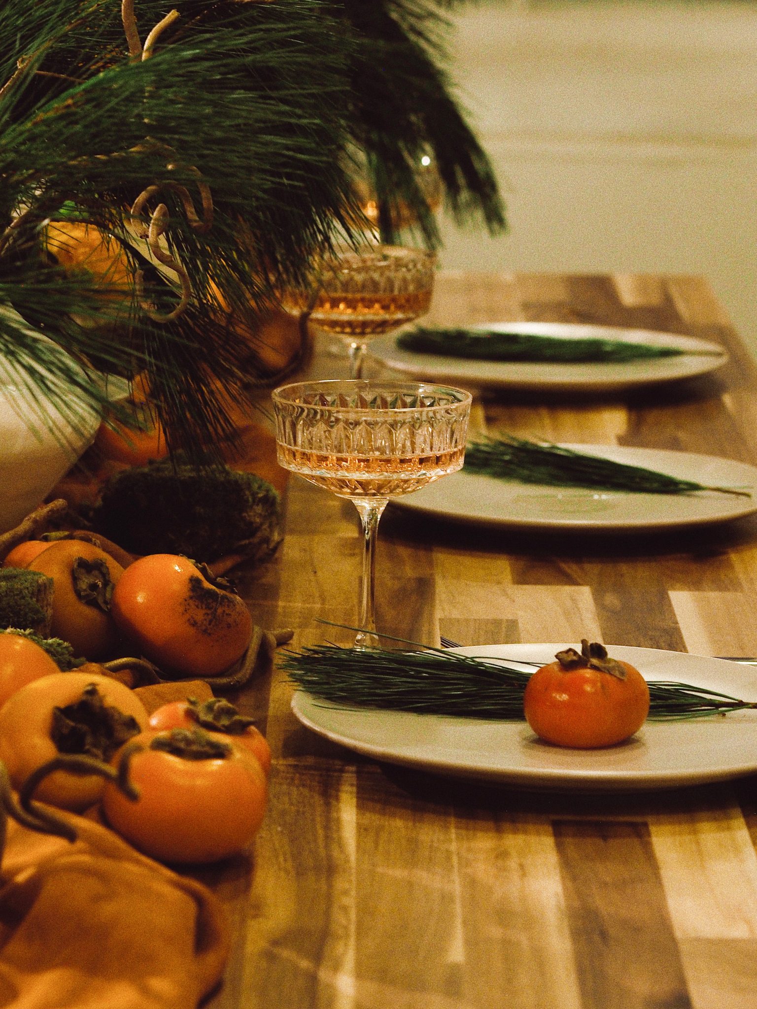 Elegant table setup with persimmons, wine glasses and pine twigs on a wooden table in Saint Petersburg.