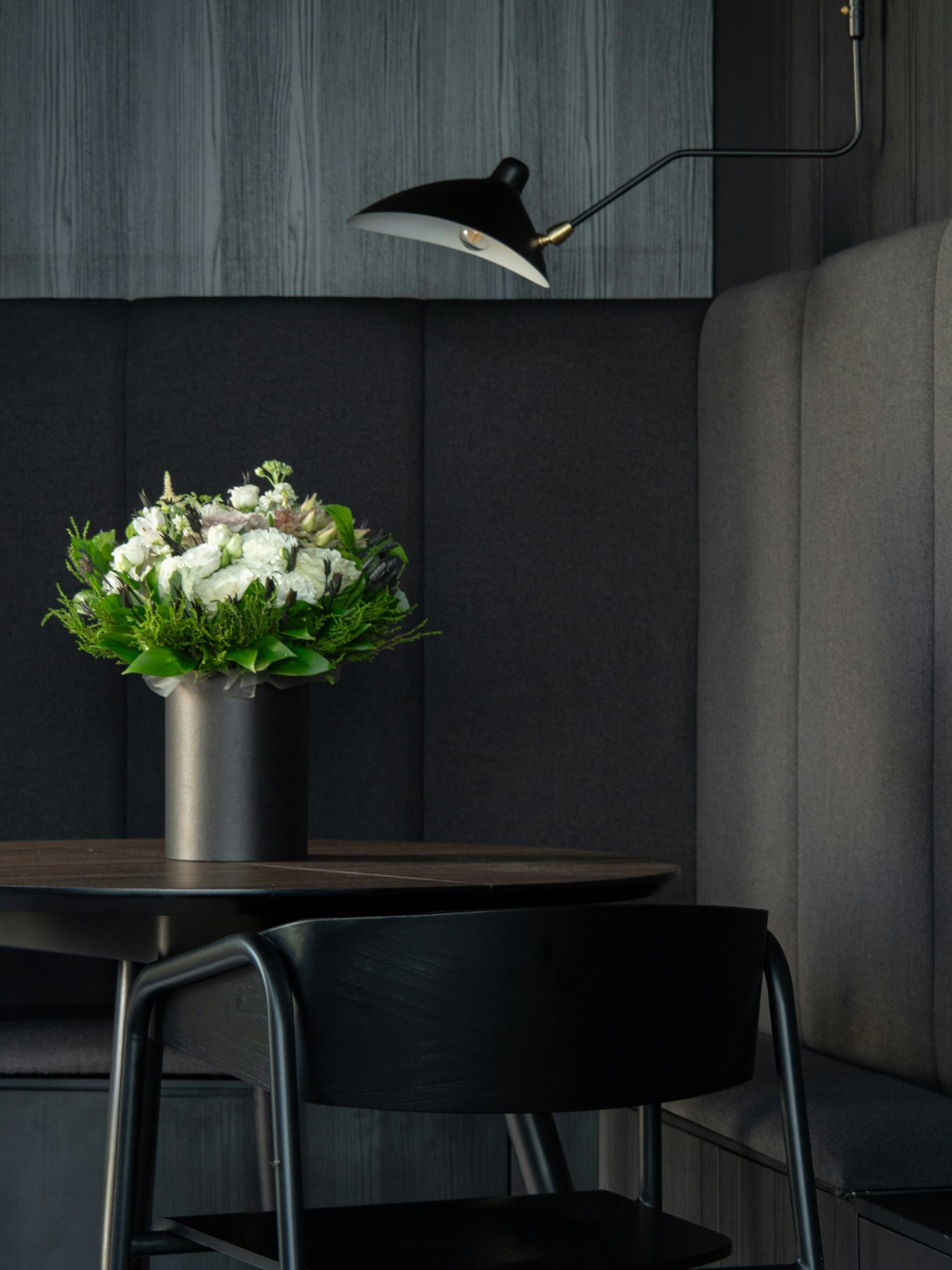Experience the allure of an elegant, dark interior as it frames a beautifully arranged bouquet on a table. Against the subtle gray backdrop, this composition adds a touch of timeless beauty to a capti