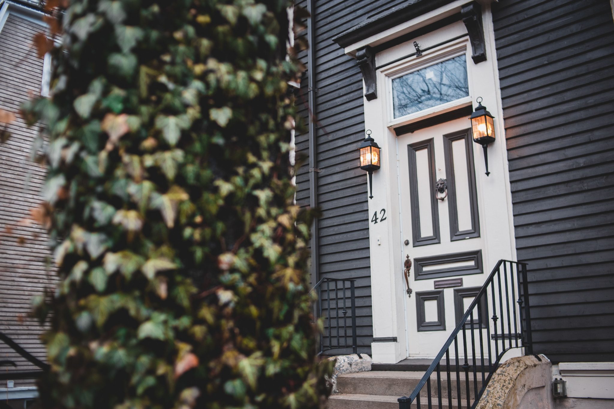 Exterior of entrance porch with white wooden door and street lamps on doorposts and stairs with black metal railings