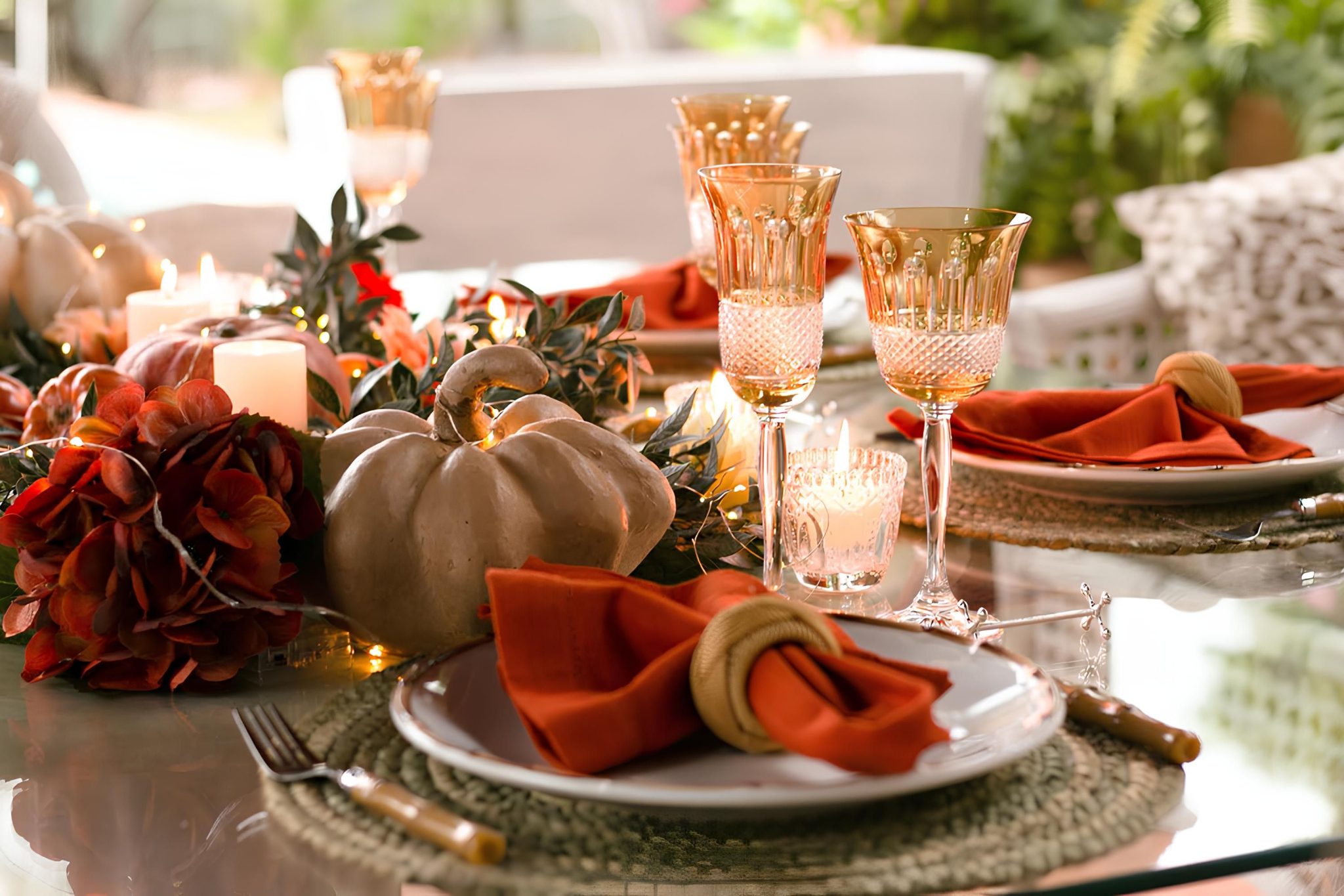 Festive autumn dining table with pumpkins, candles, and gold-rimmed glassware.