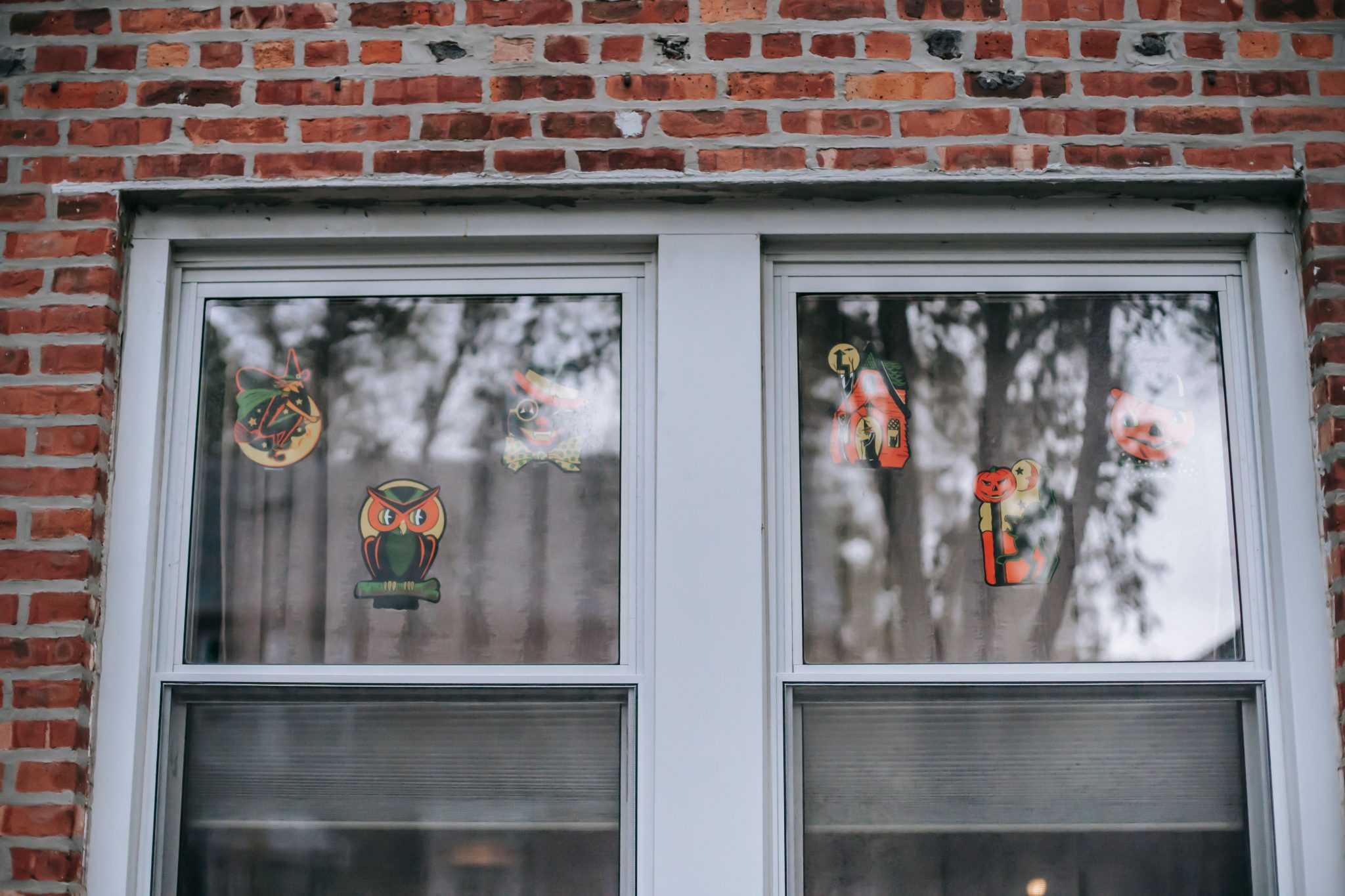 Fragment of window with various decorative elements of Halloween stickers on glass of residential building with brick wall during holiday celebration