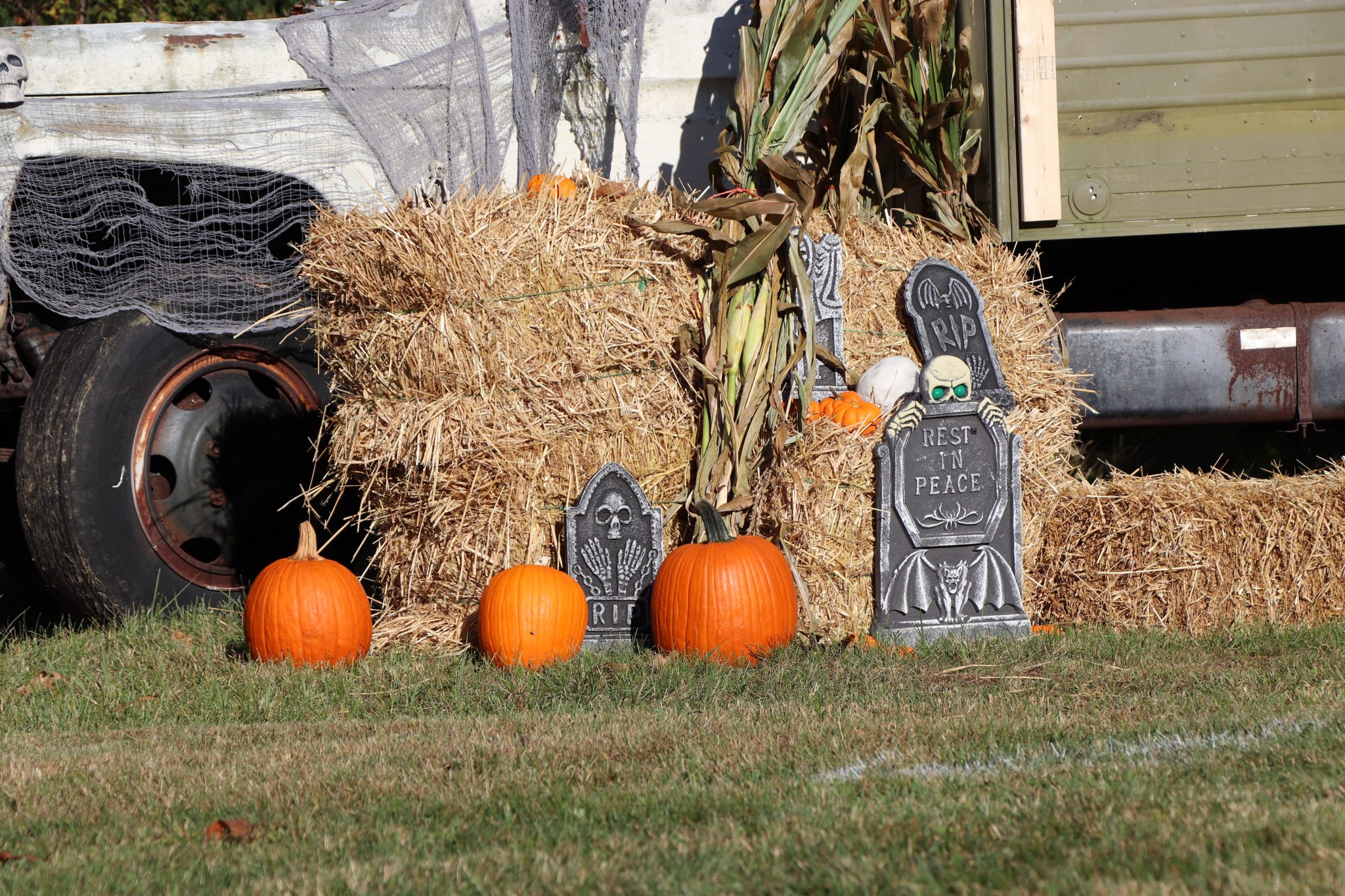 Halloween setup with pumpkins, hay bales, and tombstones in rural setting.