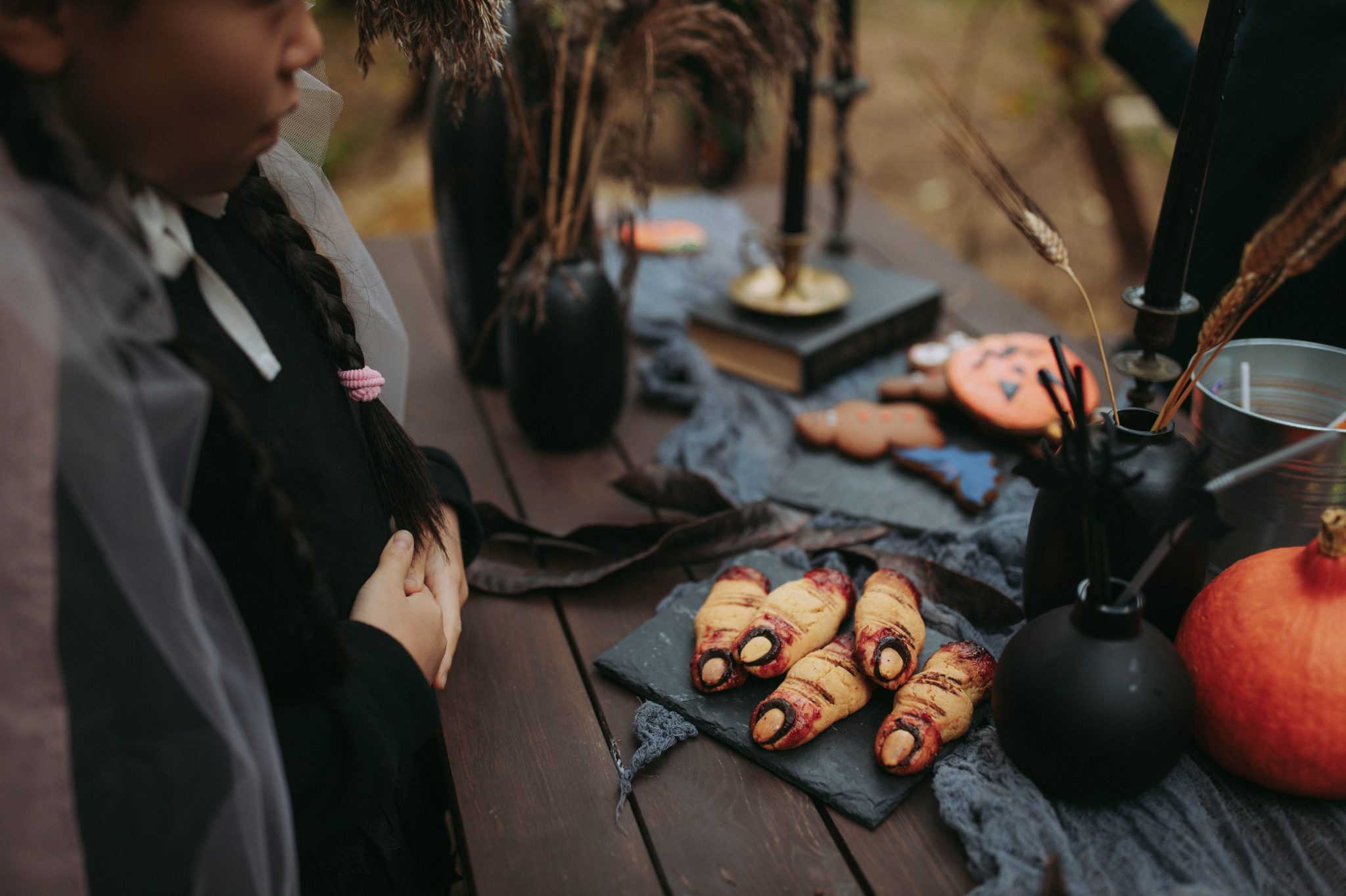Halloween themed cookies and decor on a wooden table, featuring spooky fingers and pumpkins.