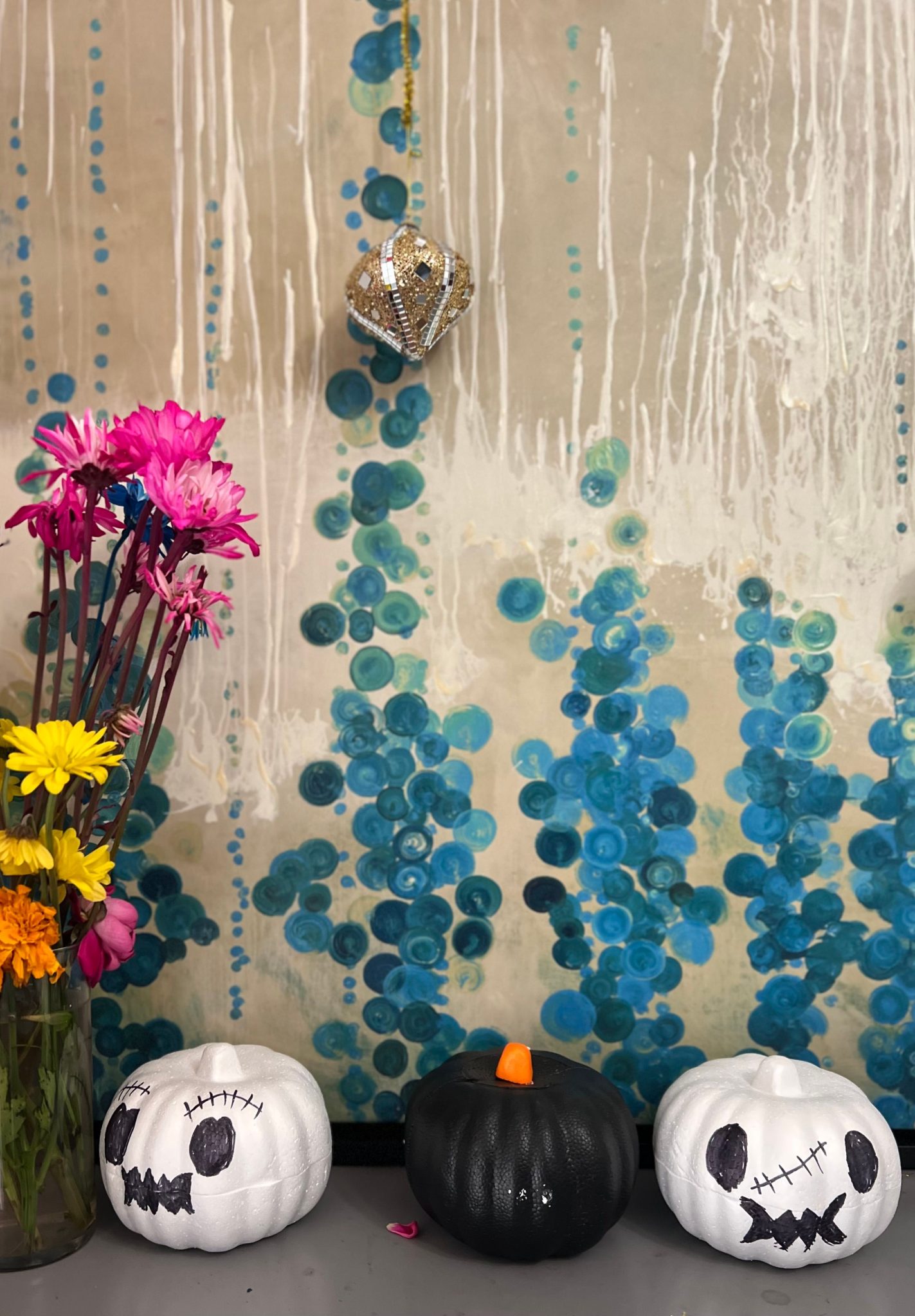 Halloween themed decoration with painted pumpkins and vibrant flowers against an artistic wall.