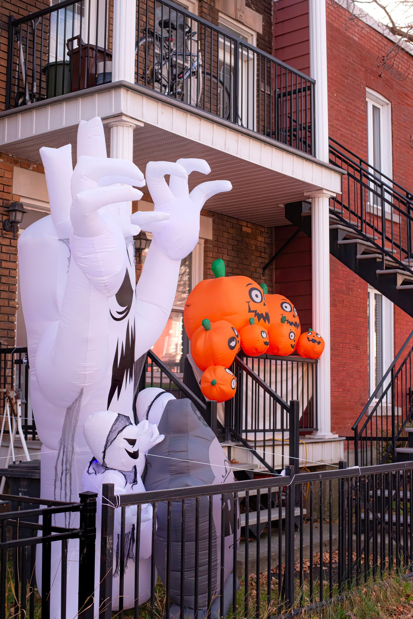 Inflatable ghost and pumpkins adorn a porch for Halloween in an urban setting.