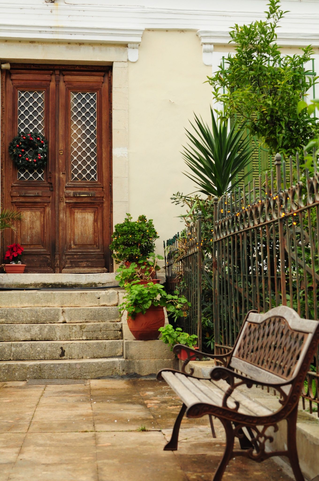 Inviting rustic entrance with wooden doors, greenery, and a decorative bench.