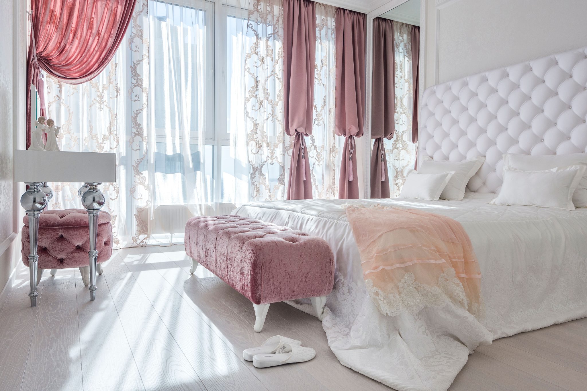 Luxury interior of white and rosy bedroom with big bed soft ottomans and elegant decor