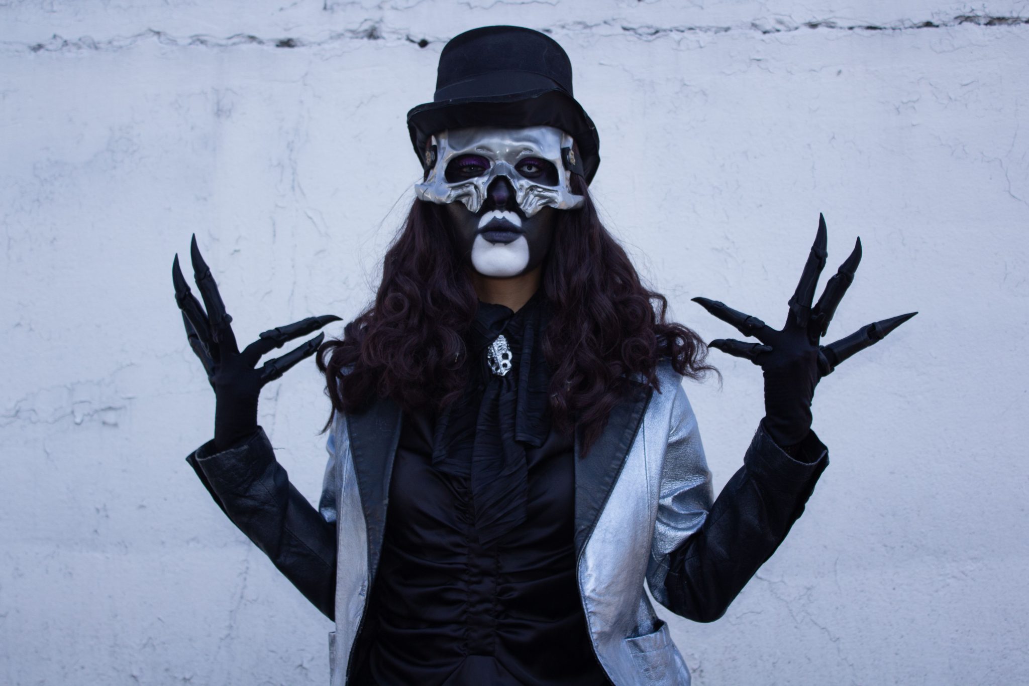 Mysterious figure in silver and black costume with skeletal mask and top hat.