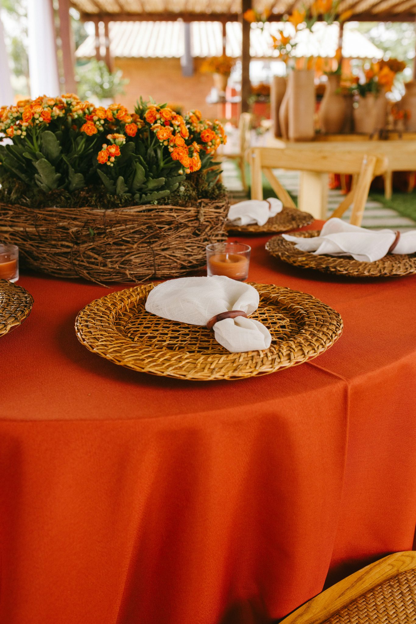 Orange tablecloth with woven placemats, white napkins, and orange flowers