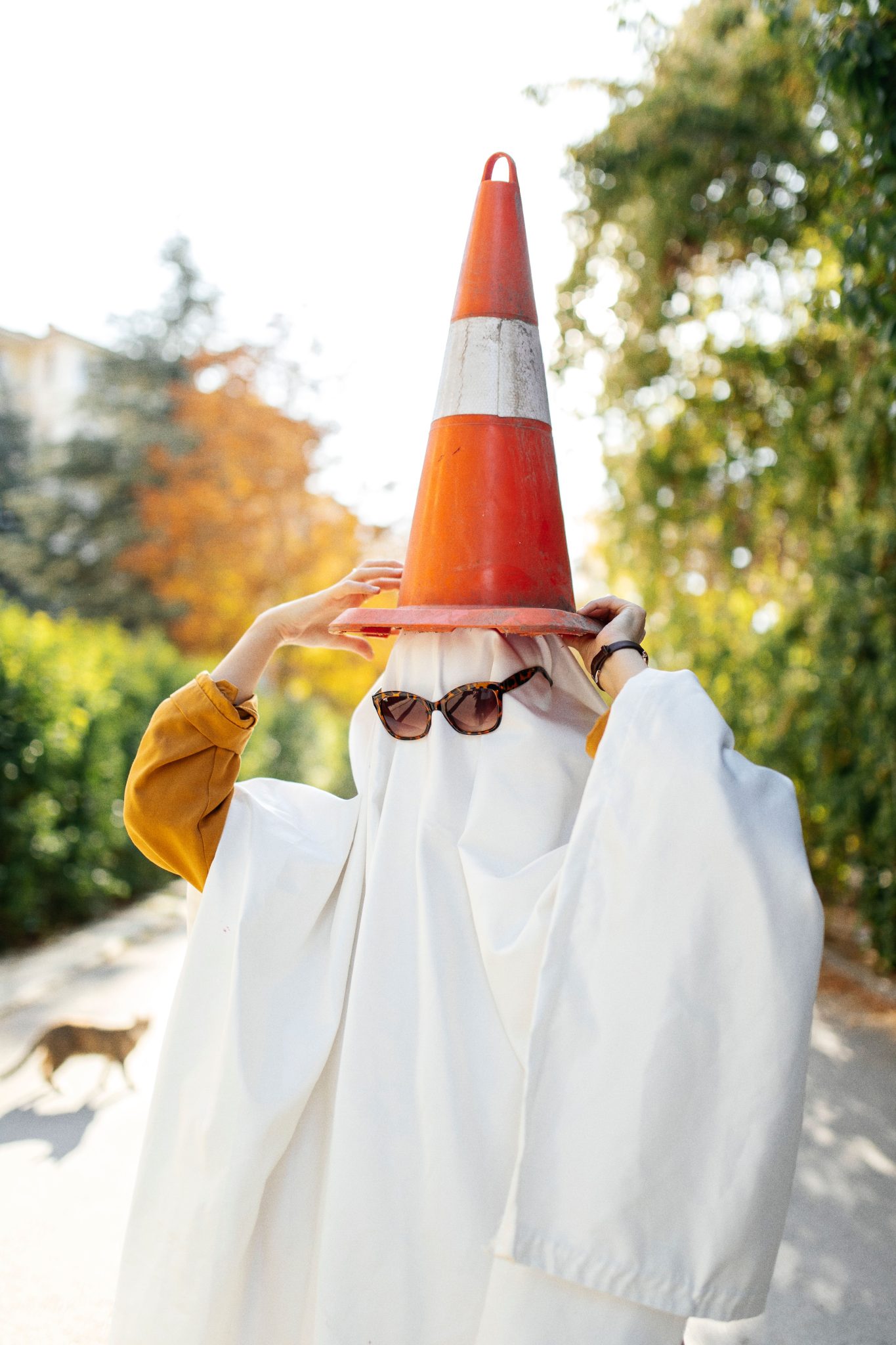 Person dressed as ghost with cone hat walking outdoors on a sunny day.