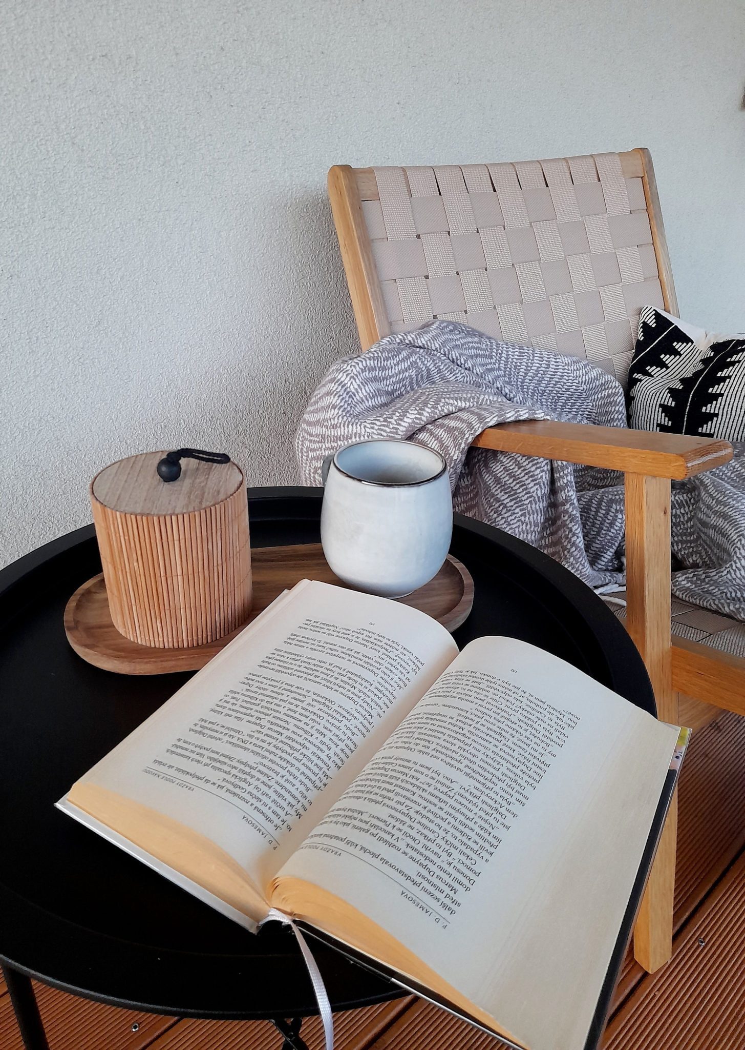 Relaxing corner with a book, mug, and a cozy blanket in a chair.