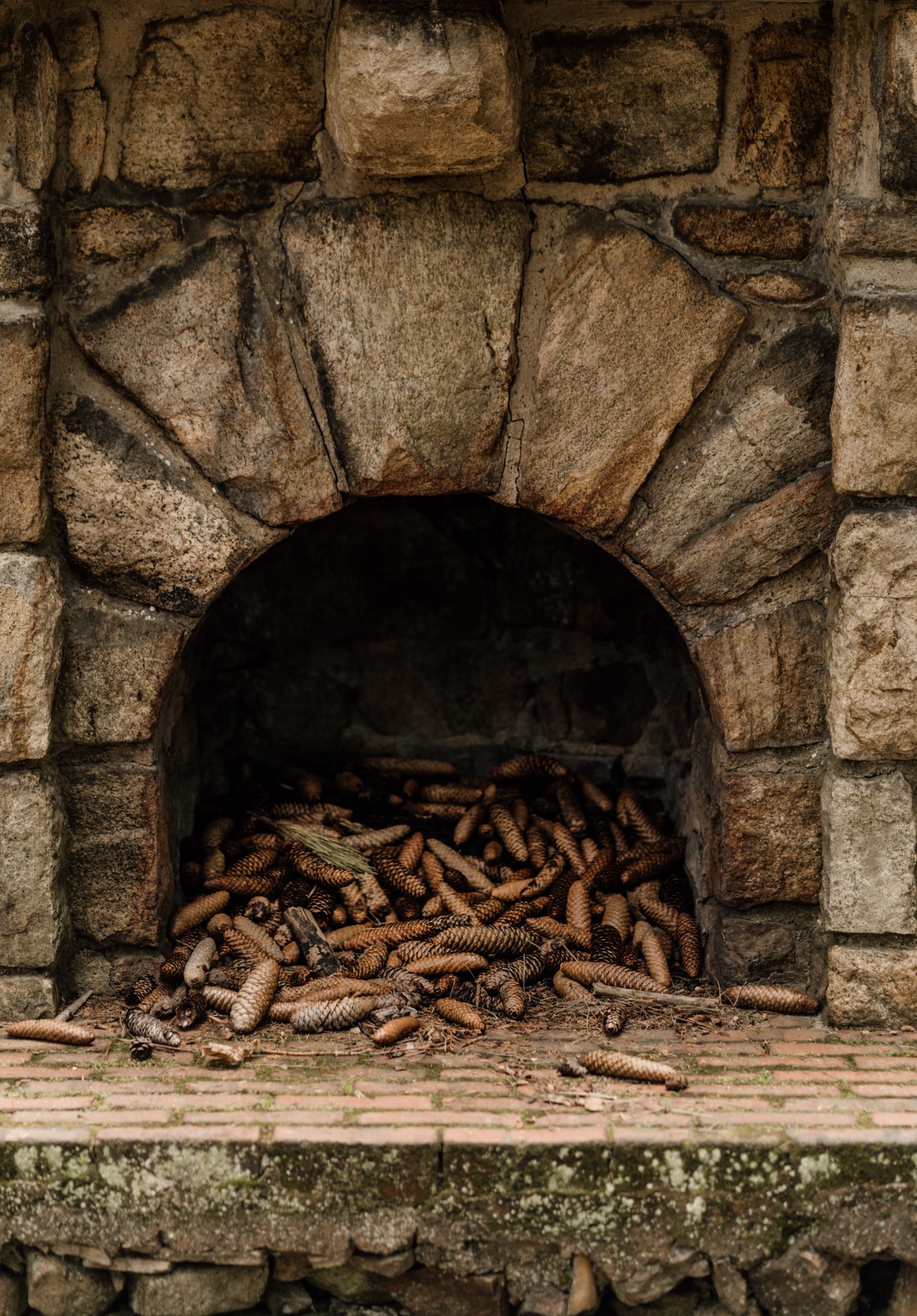 Rustic stone fireplace filled with pine cones, offering a natural, outdoor aesthetic.