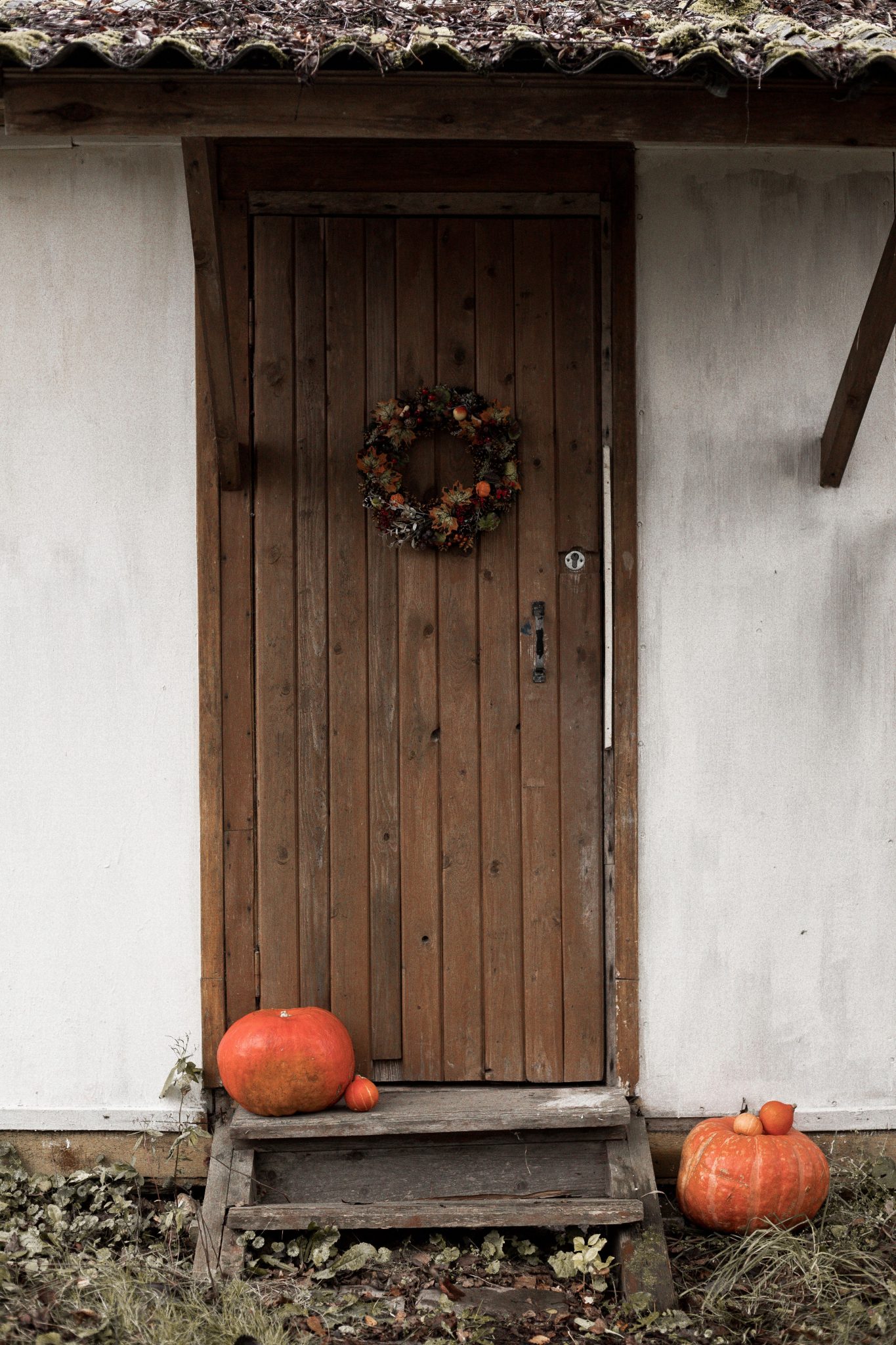 Rustic wooden door decorated with autumn wreath and pumpkins for Halloween celebration.