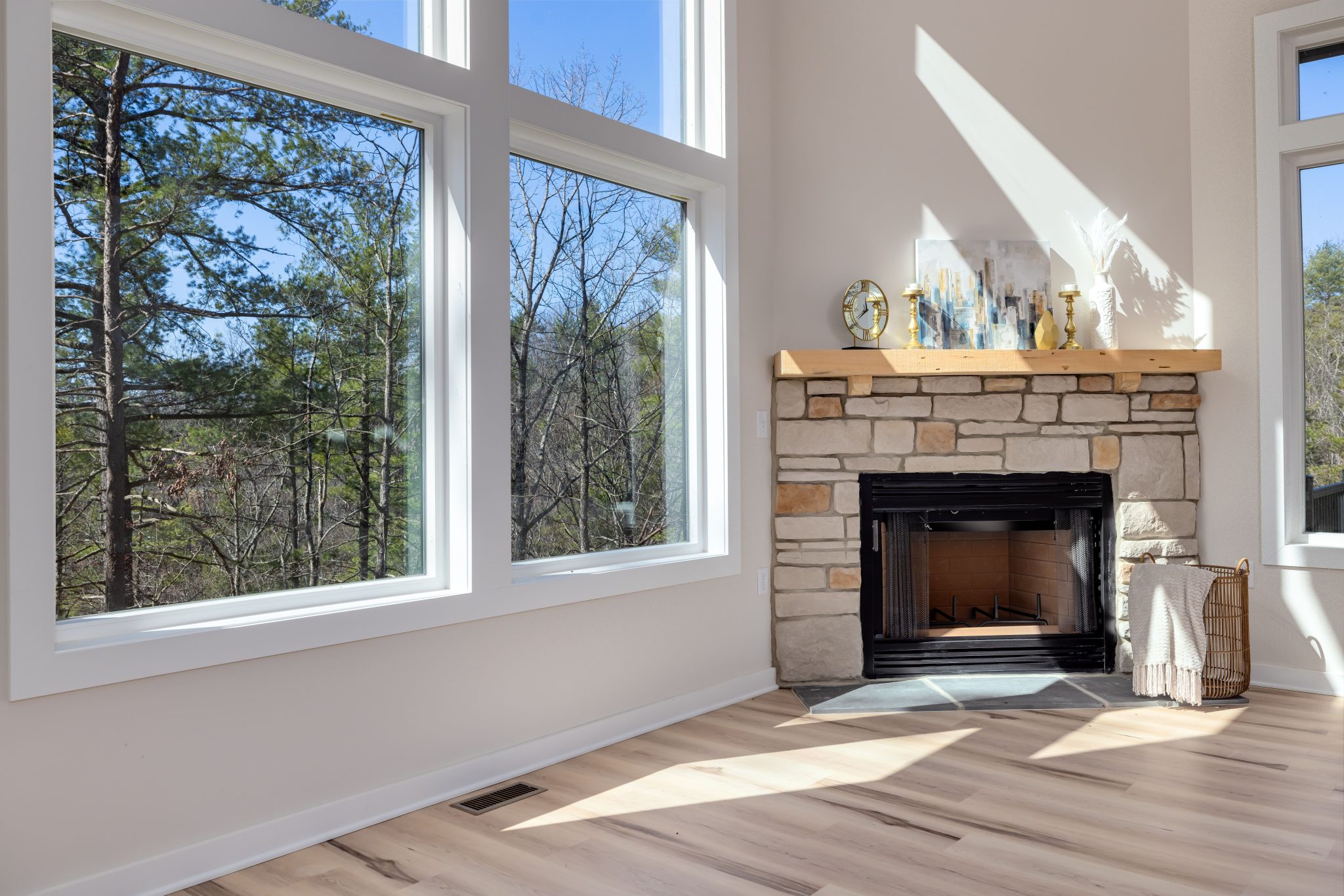 Spacious modern living room featuring large windows and a stone fireplace mantel.