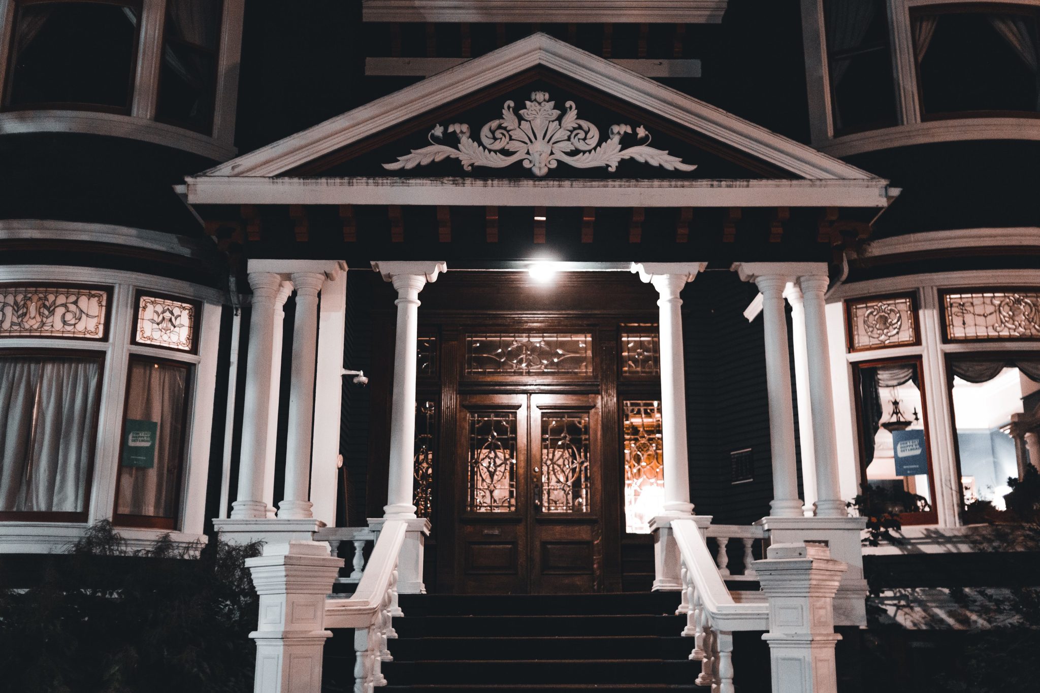 Stunning illuminated entrance of a Victorian mansion showcasing intricate architectural design at night.
