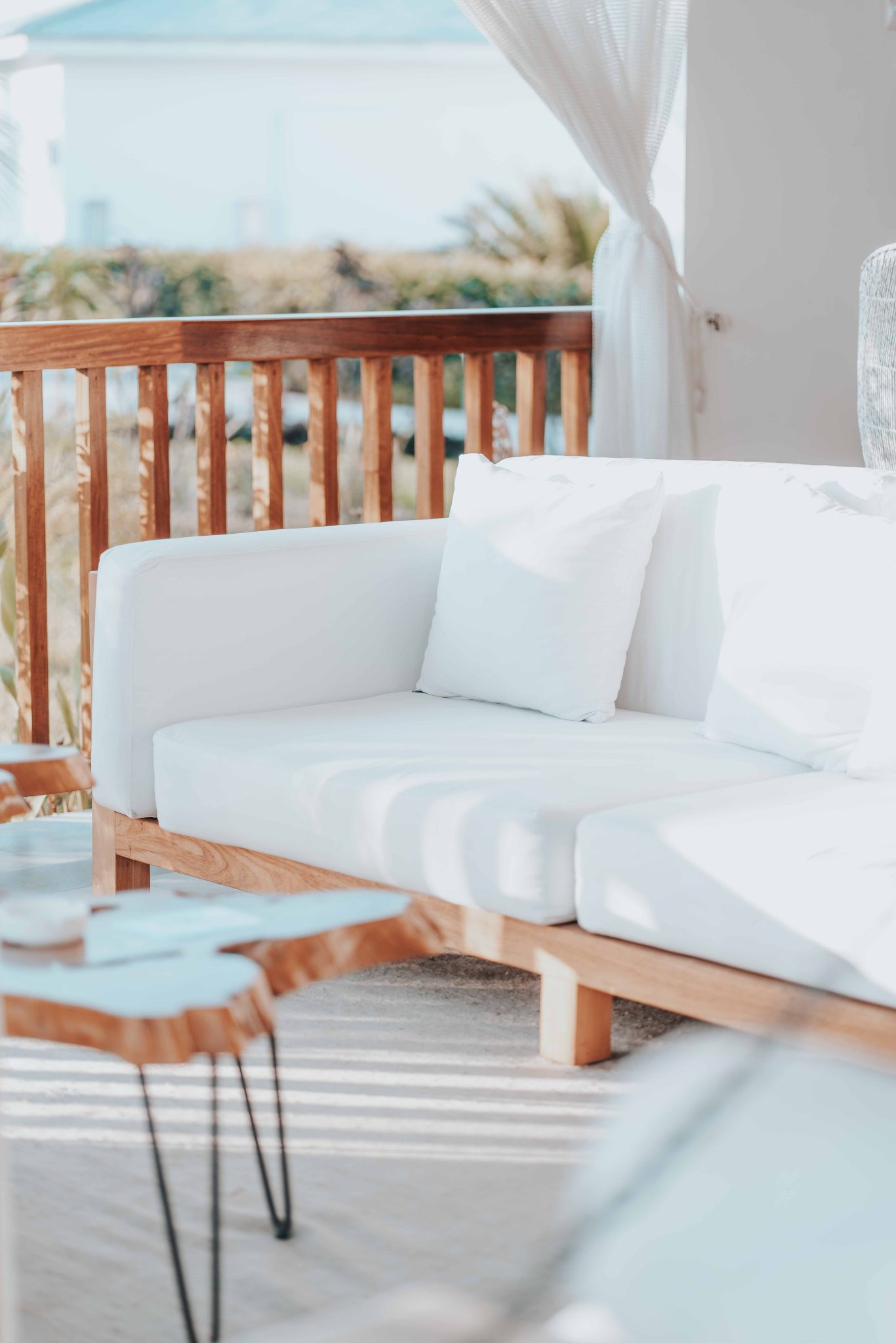 Stylish outdoor patio with white sofa and wooden furniture in bright sunlight.
