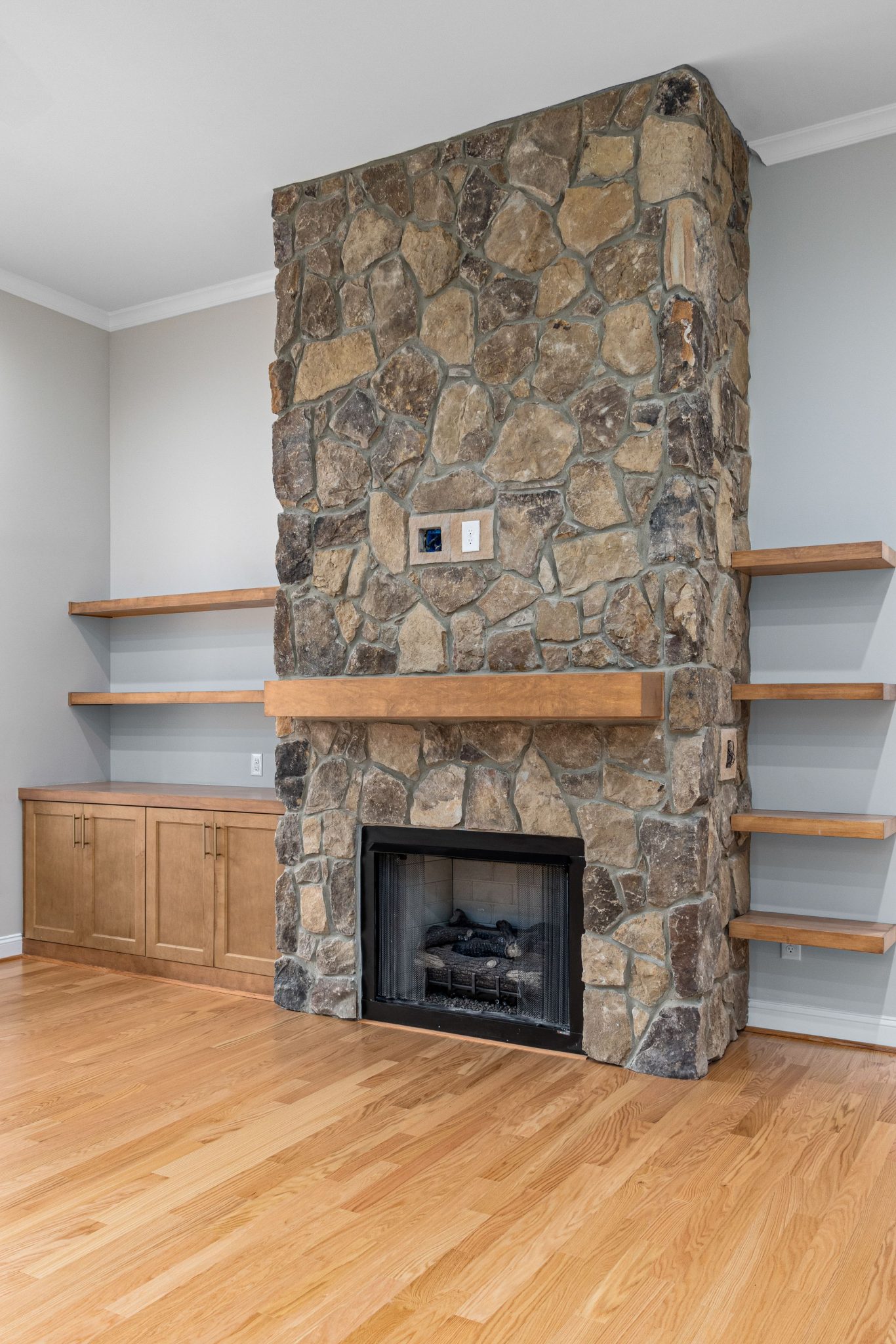 Stylish stone fireplace in a modern living room with wooden flooring and shelves.