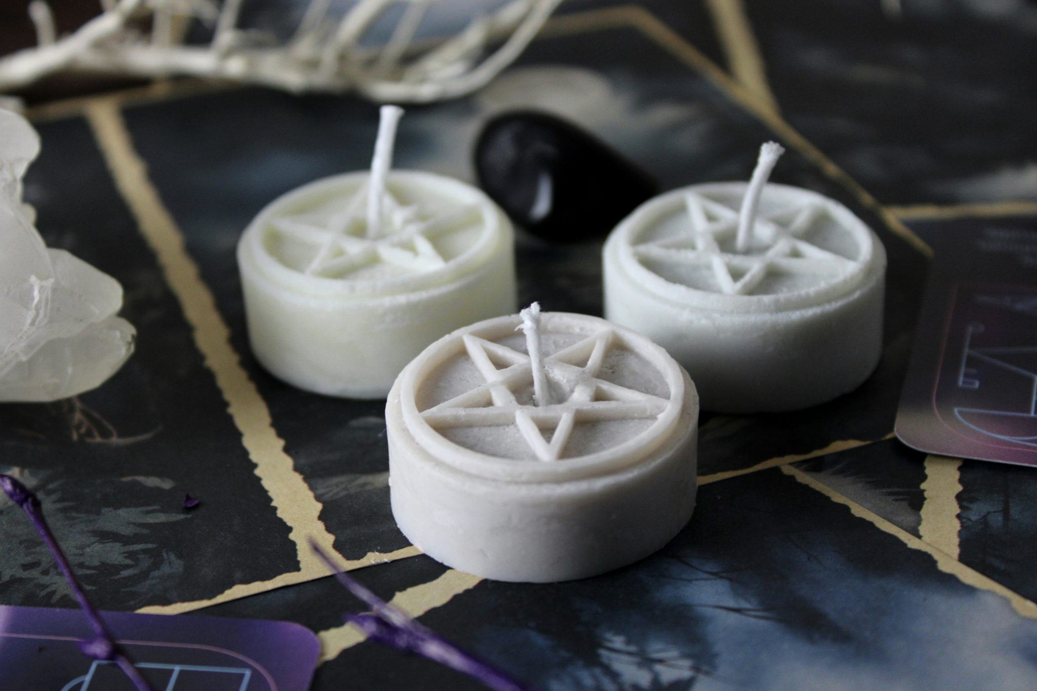 Three white wax candles with pentagram symbols on a dark surface