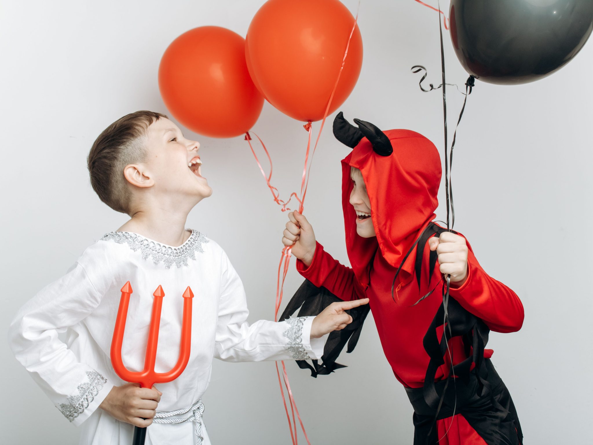 Two children in angel and devil costumes joyfully holding balloons for Halloween.