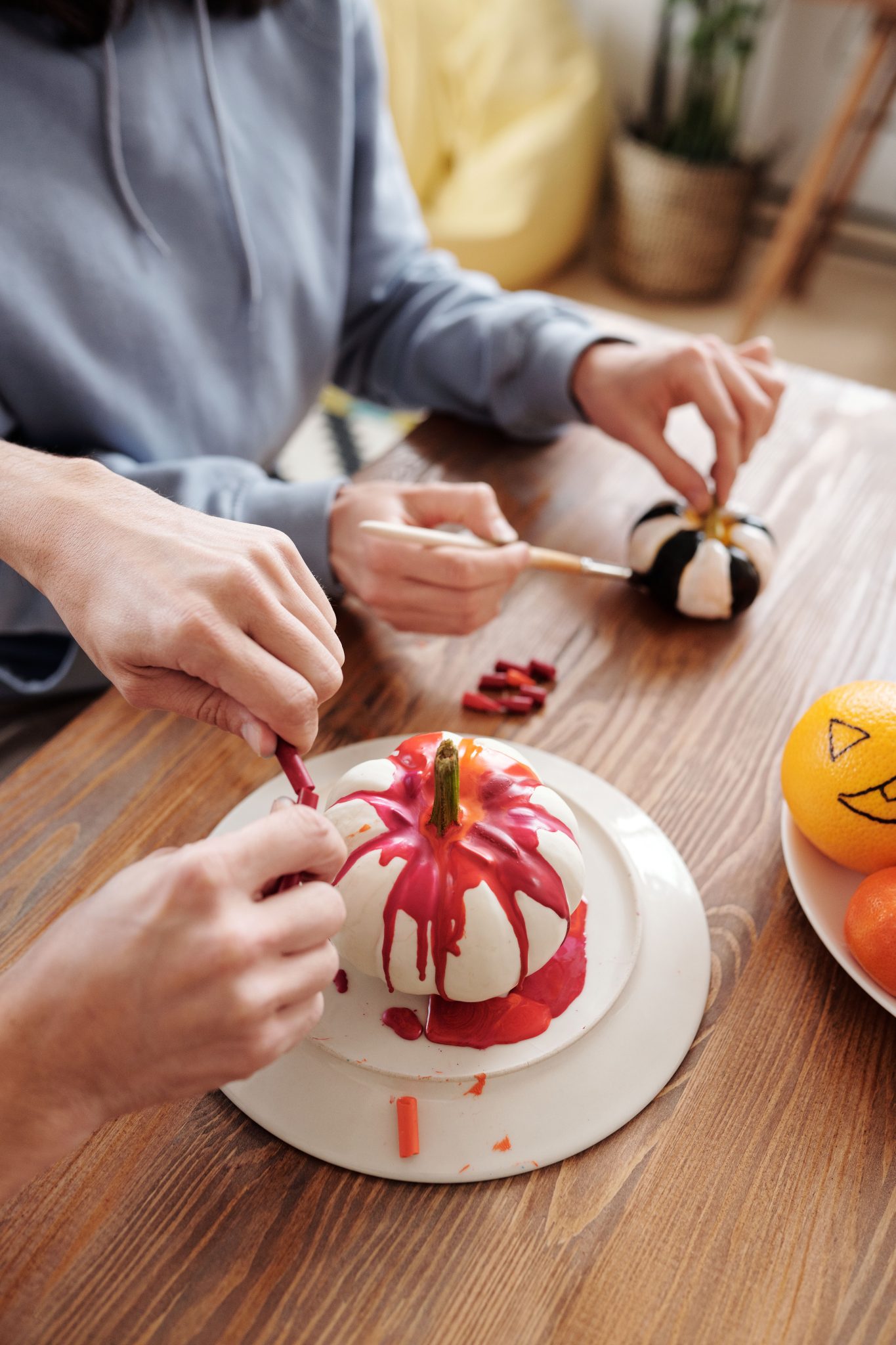 Two people decorating pumpkins with paint indoors, capturing Halloween creativity.