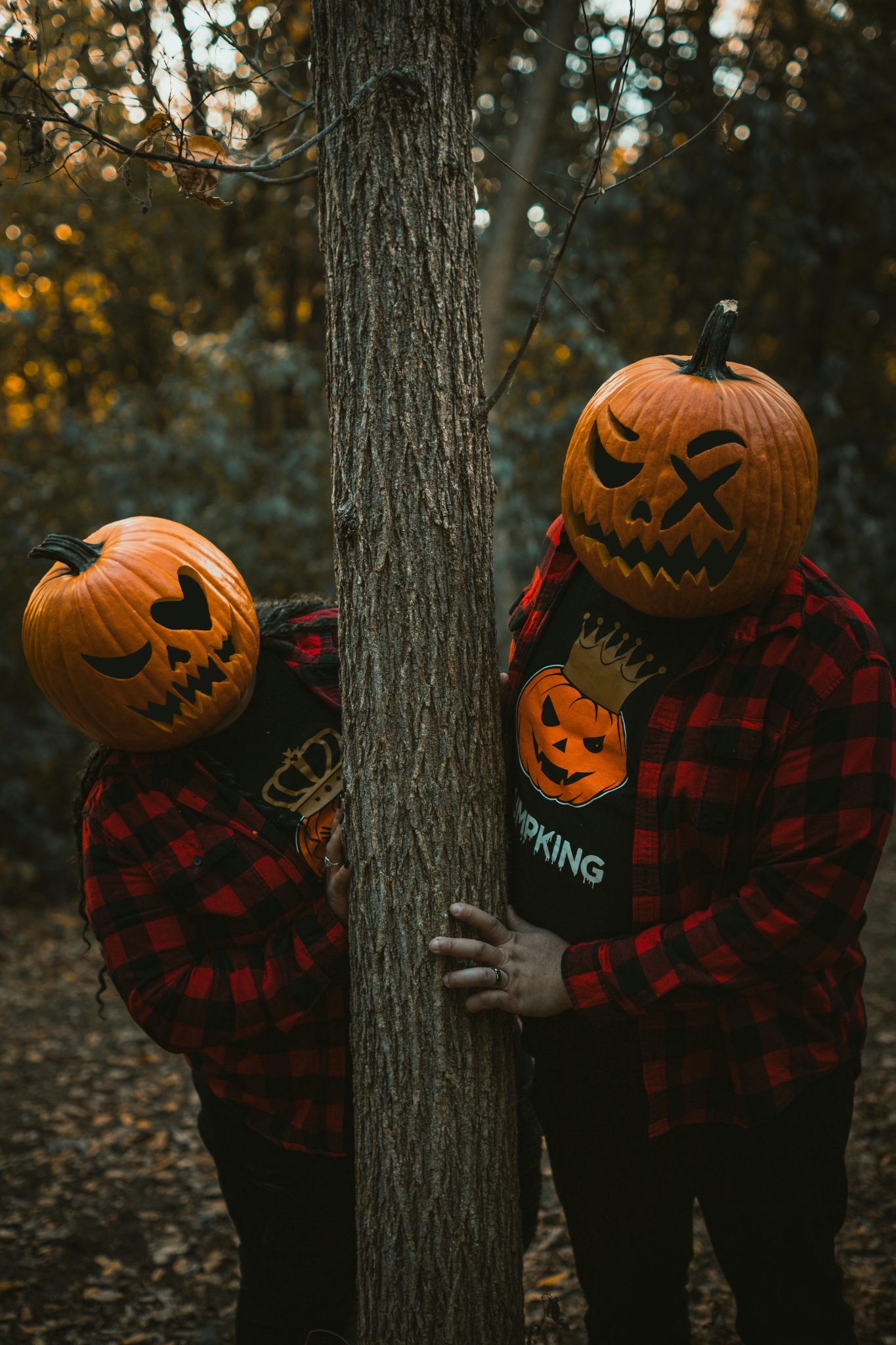 Two people with carved pumpkin heads behind a tree