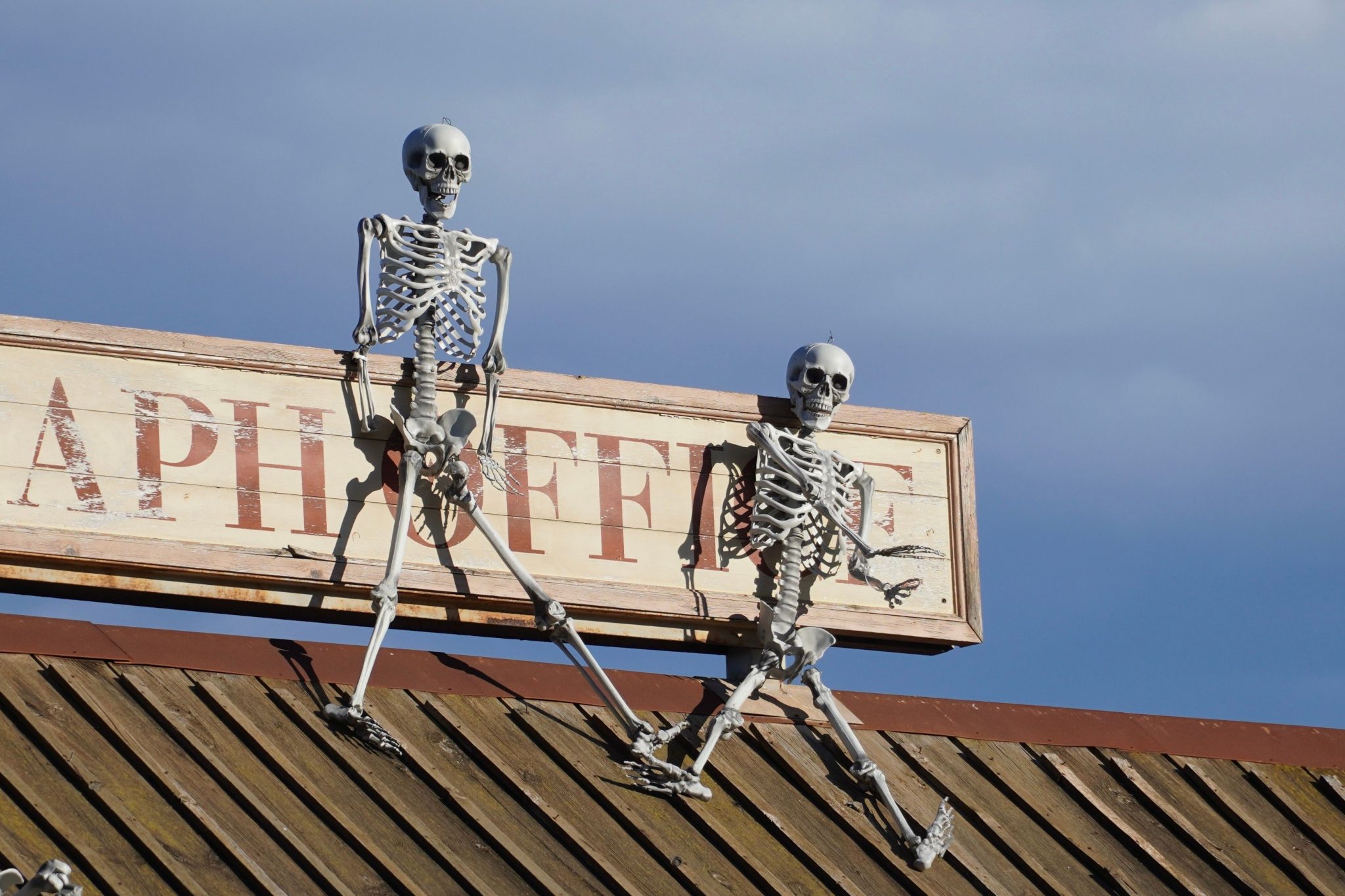 Two skeleton figures positioned on a rooftop sign set against a clear blue sky.