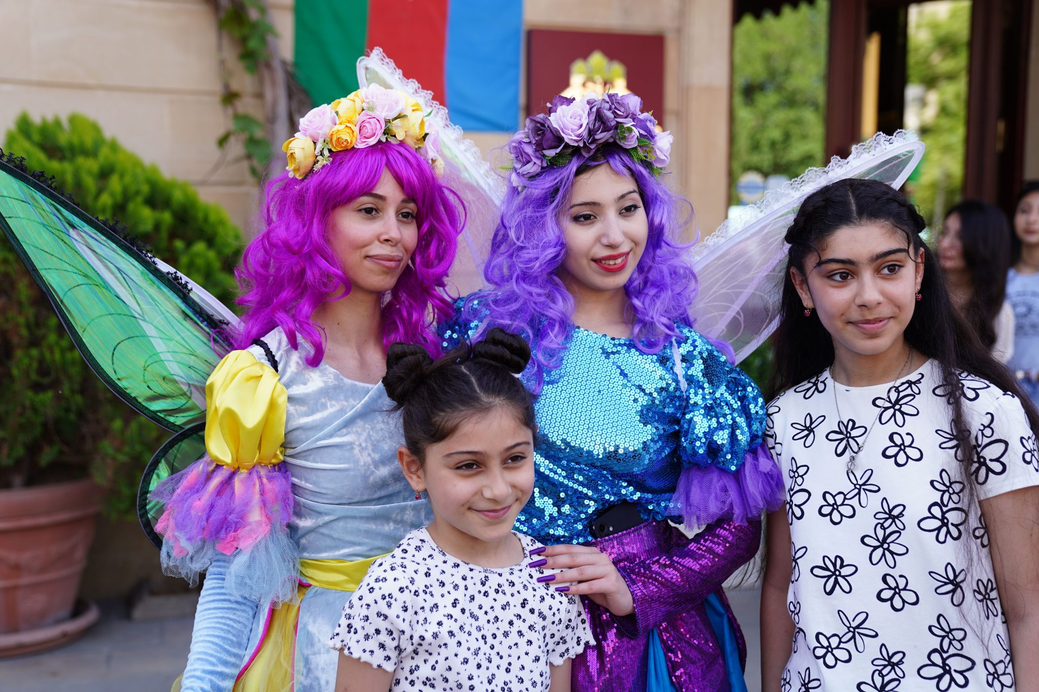 Two women in vibrant fairy costumes pose with two girls outdoors.