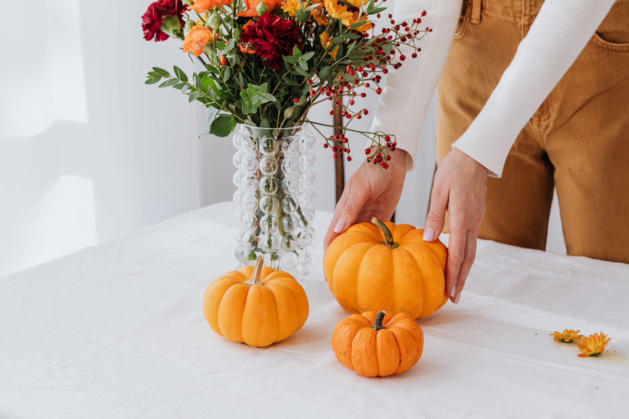 Vibrant autumn display of pumpkins and flowers on a table with white cloth.