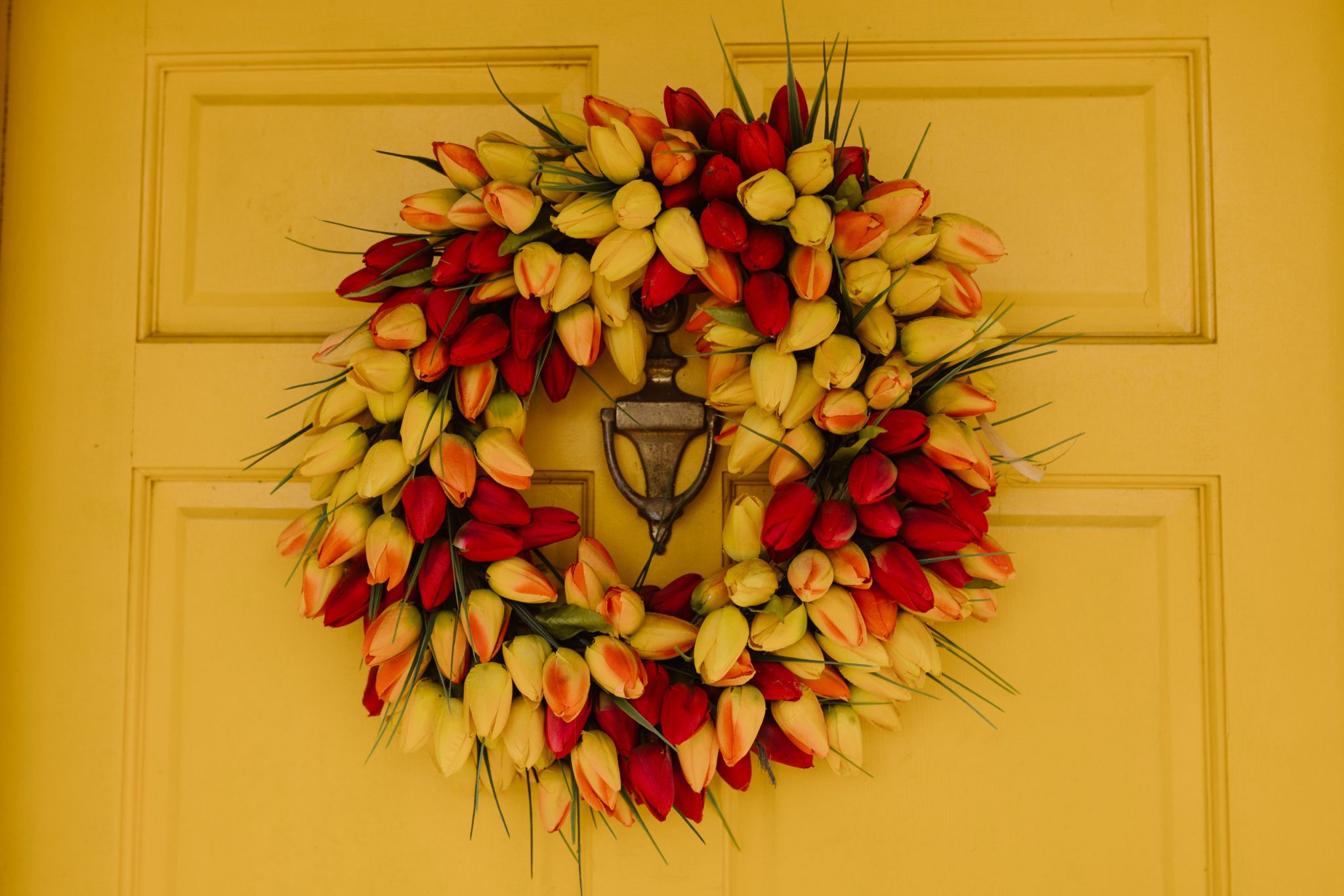 Vibrant red and yellow tulip wreath adorns a yellow front door, adding a festive touch.
