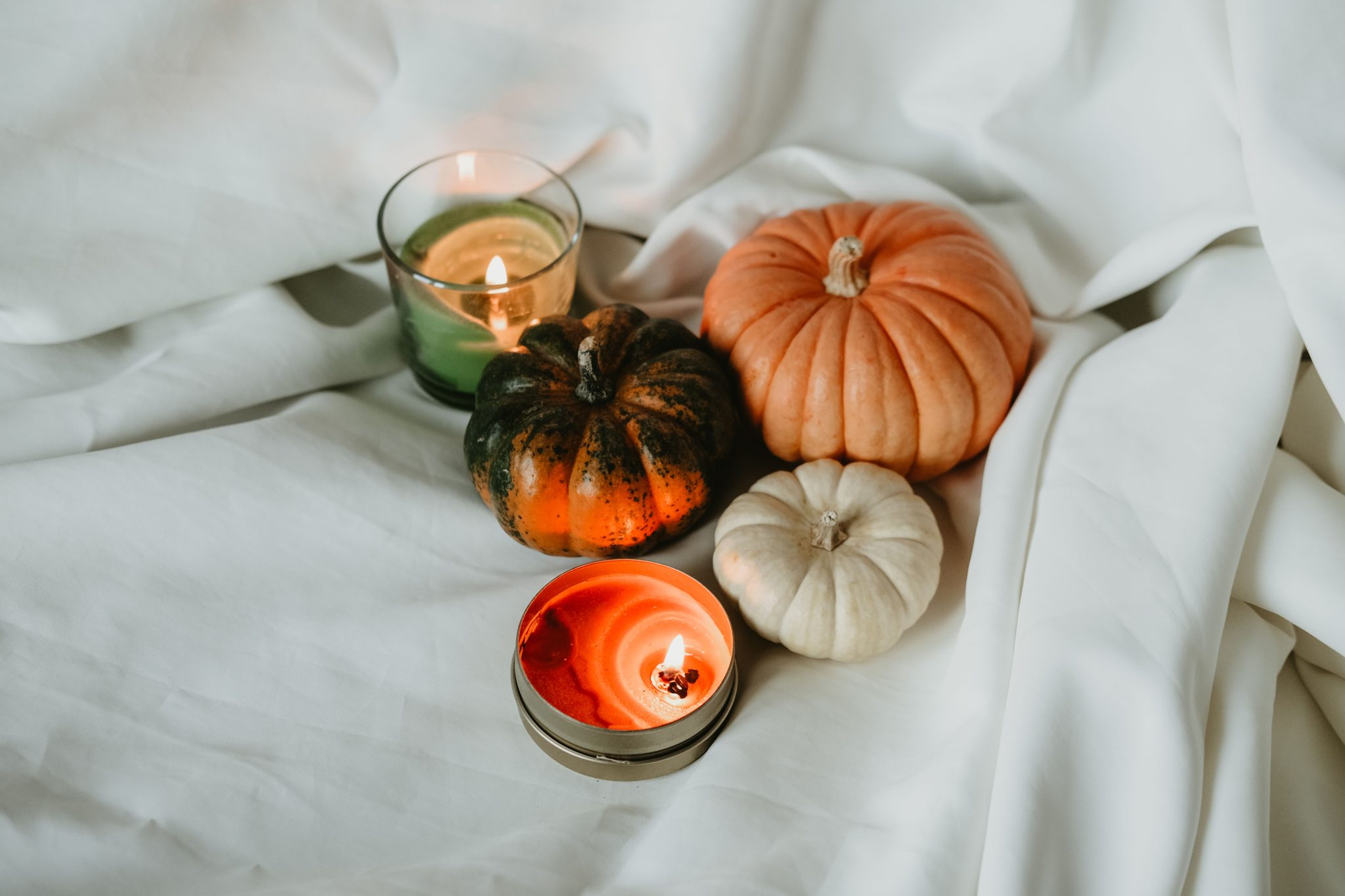 Warm ambiance with pumpkins and candles on a white sheet, perfect for fall-themed occasions.