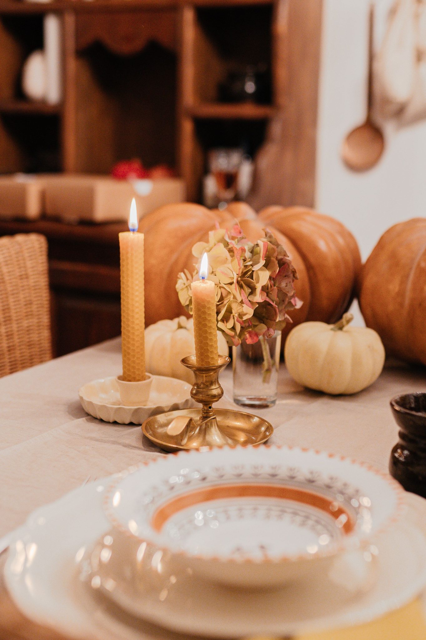 Warm and inviting fall table setting with candles, pumpkins, and dishes in a cozy indoor setting.