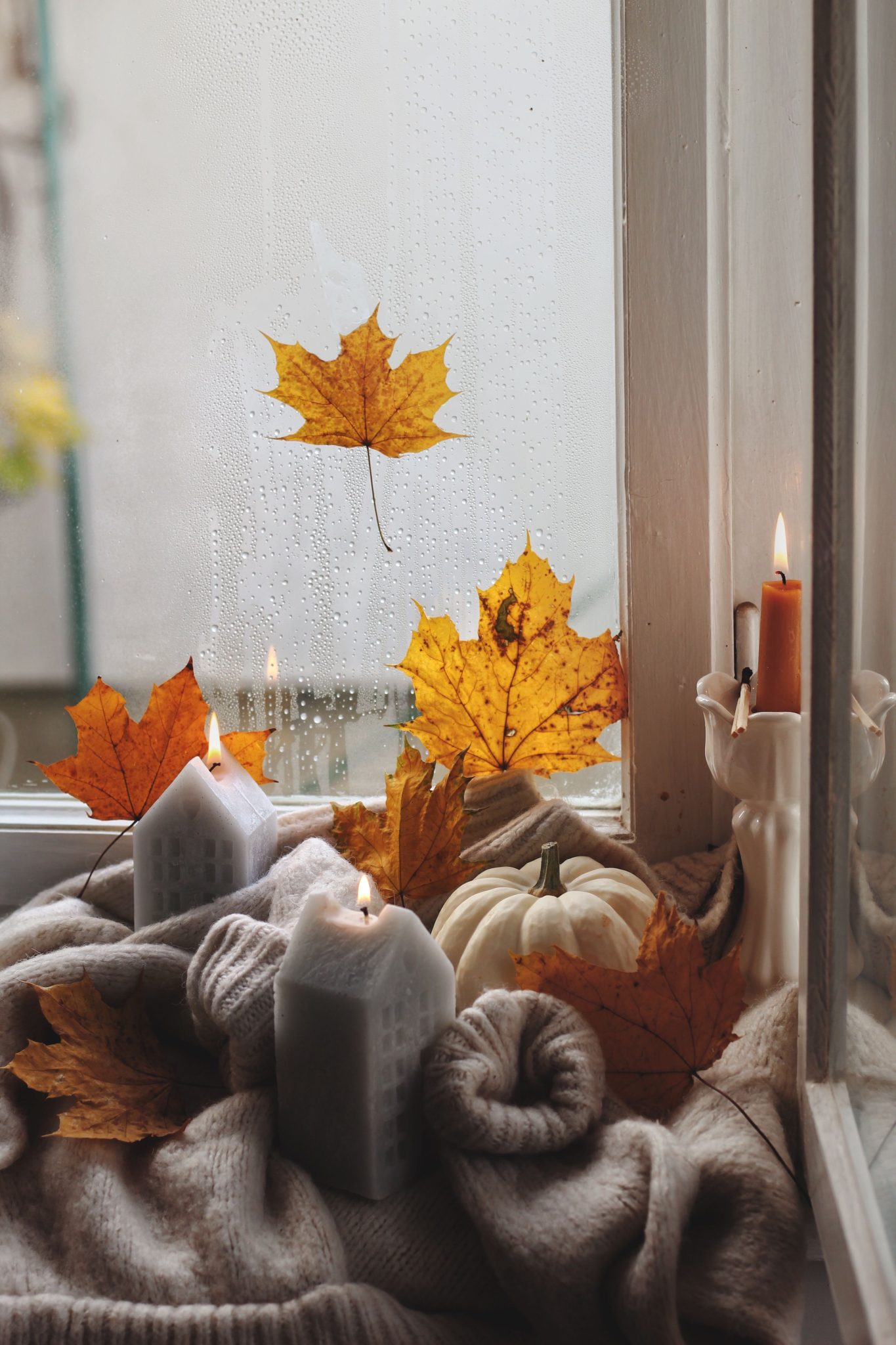 Warm autumn atmosphere with candles, leaves, and pumpkins on a cozy windowsill.
