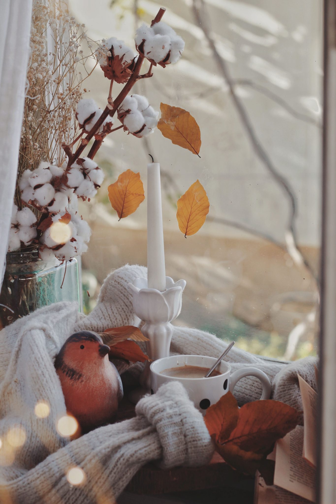 Warm autumn scene with a candle, coffee, and leaves for cozy vibes.