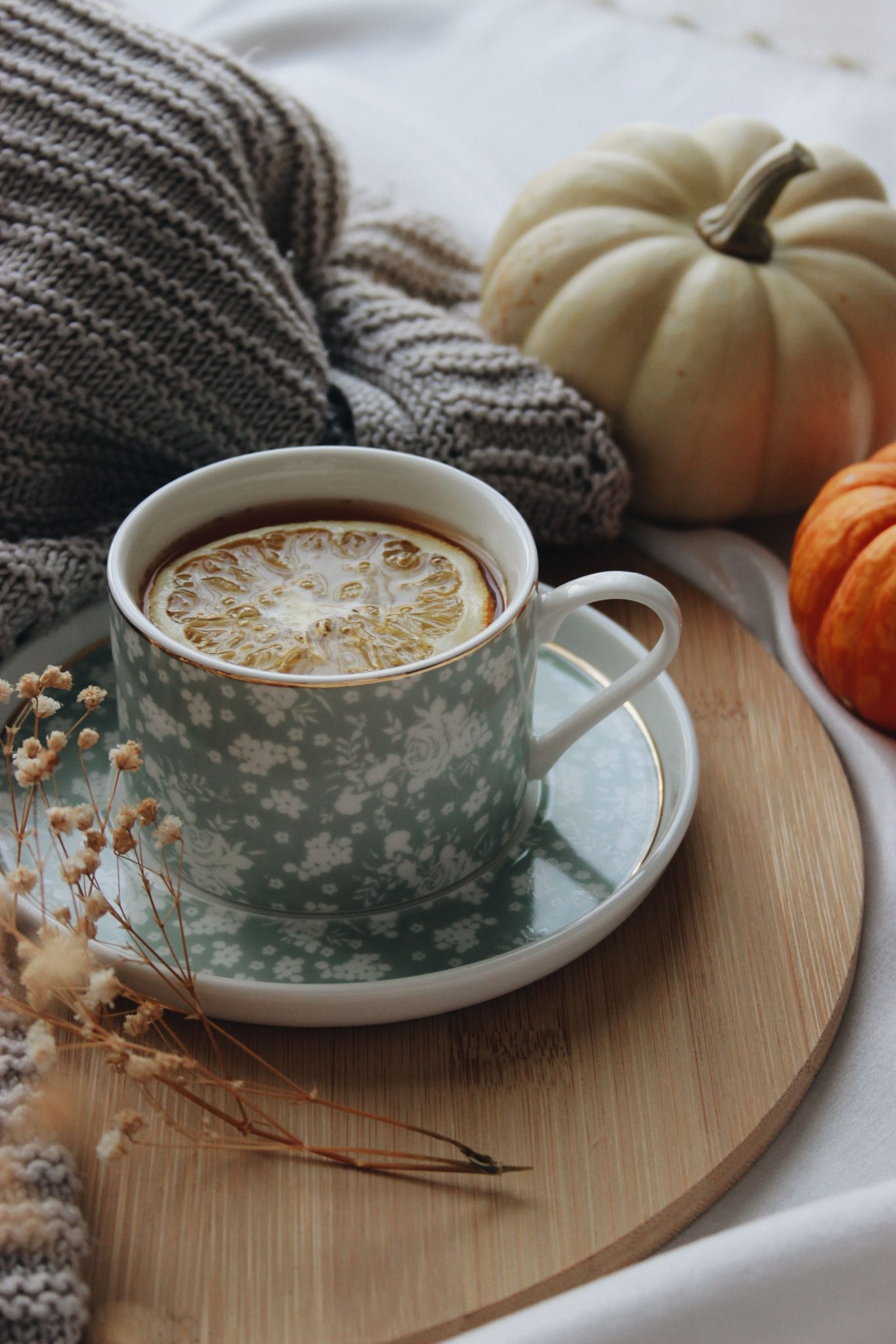 Warm autumn scene with a cup of tea, lemon slice, and pumpkins on a cozy blanket.